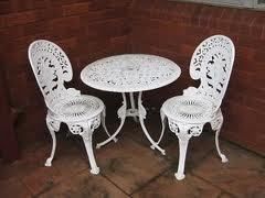 White ornate cast iron bistro set with a round table and two chairs on a brick patio.