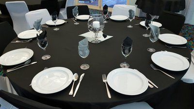 A round table set for a formal event, with white plates, black napkins, and glassware.