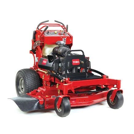 A red Toro stand-on commercial lawn mower, angled to show its engine, large tires, and cutting deck on a white background.
