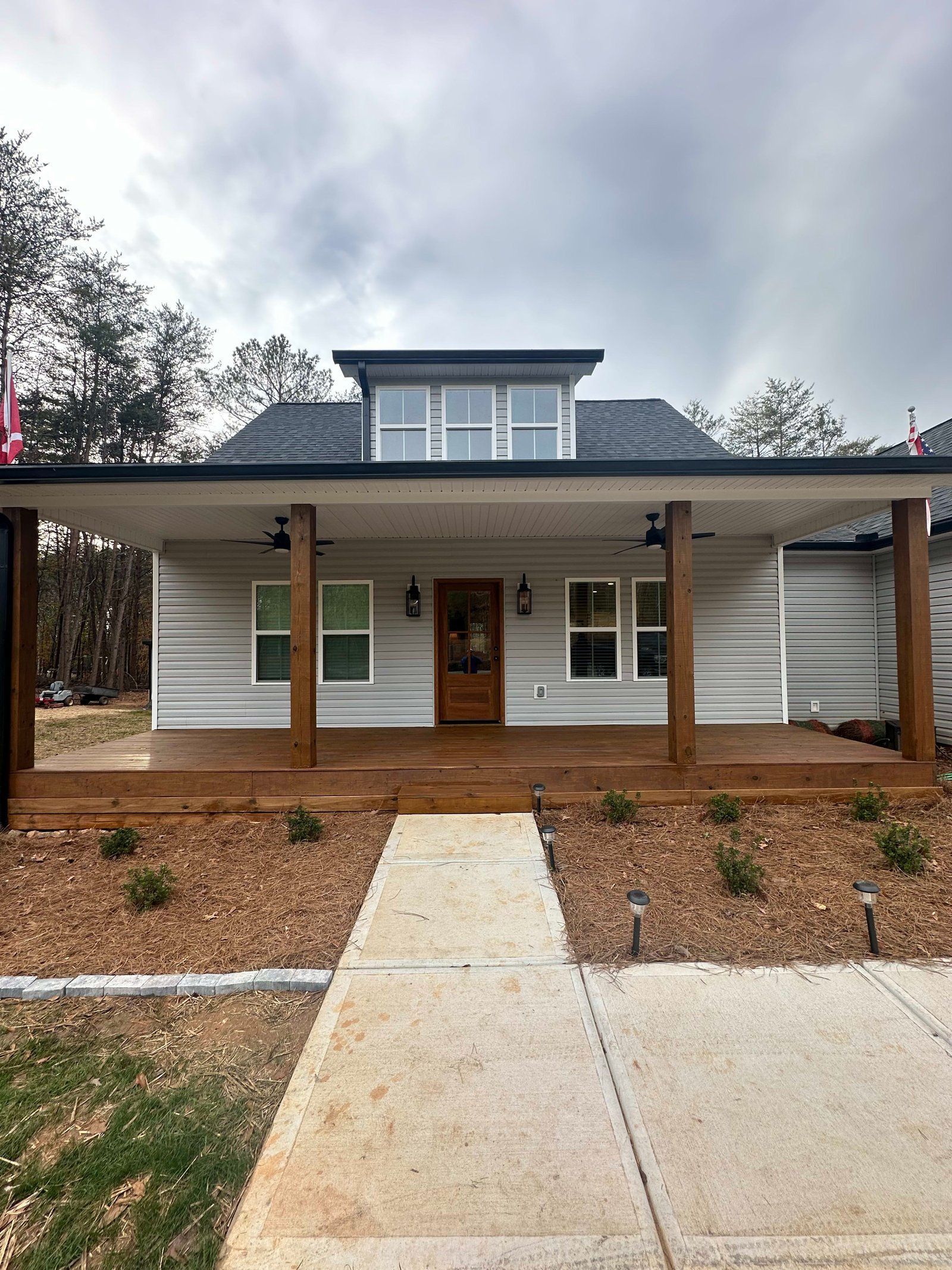 A light gray house with a covered porch, brown wooden pillars, and a pathway leading to a front door.