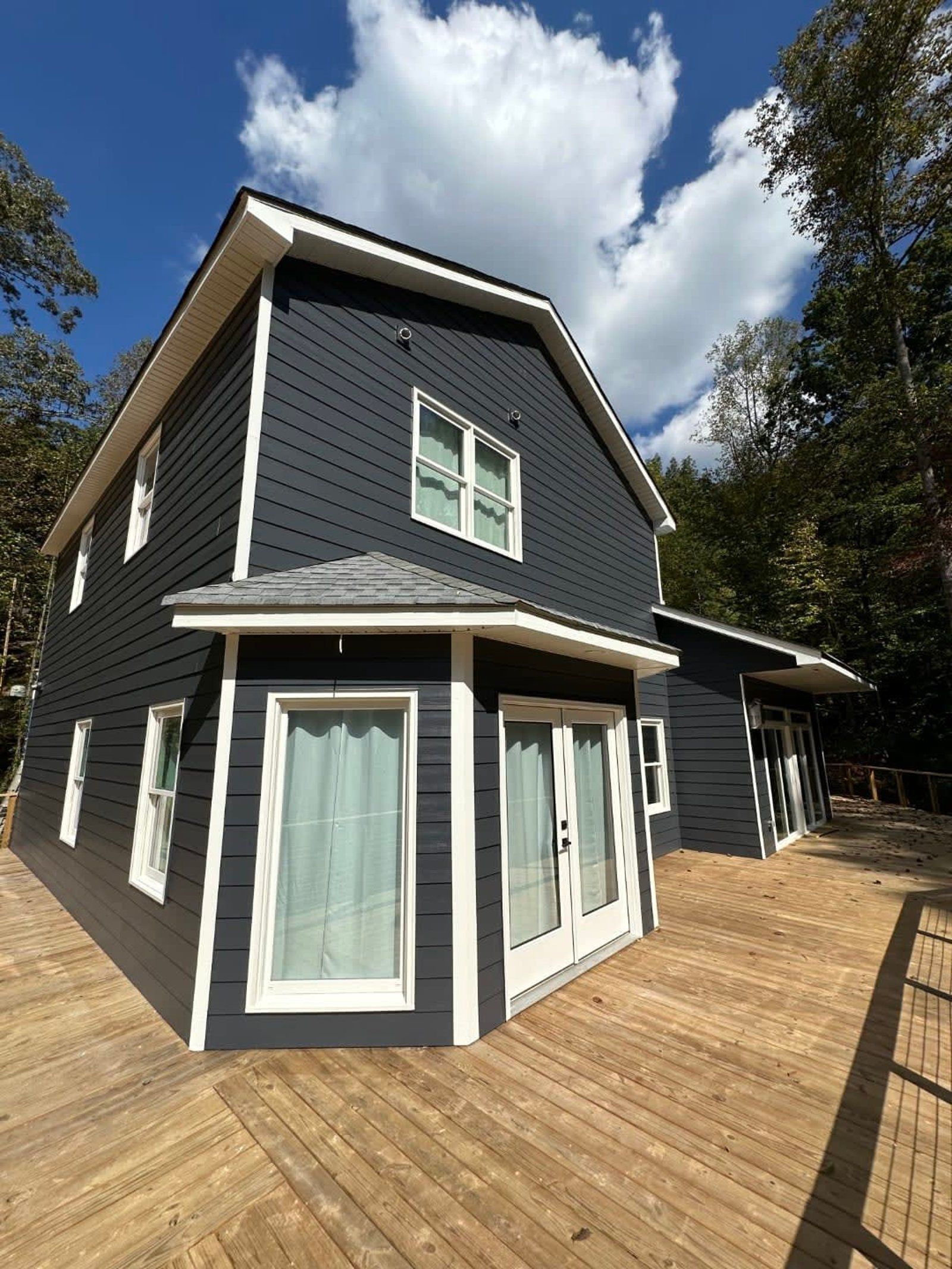 Dark blue house with white trim and deck under a cloudy blue sky.
