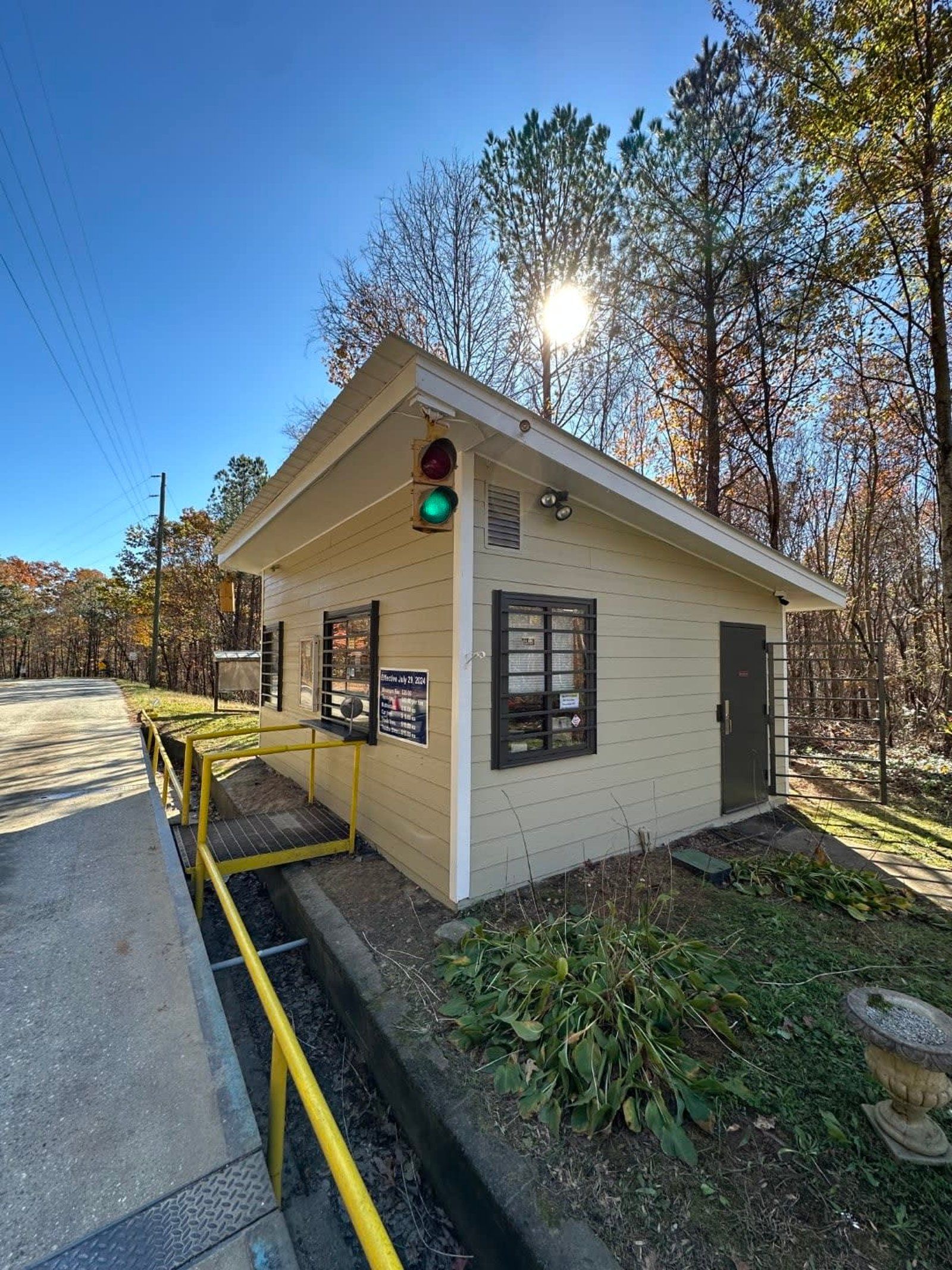 Small beige booth with green light, yellow railing, and window, in a sunny outdoor setting with trees.