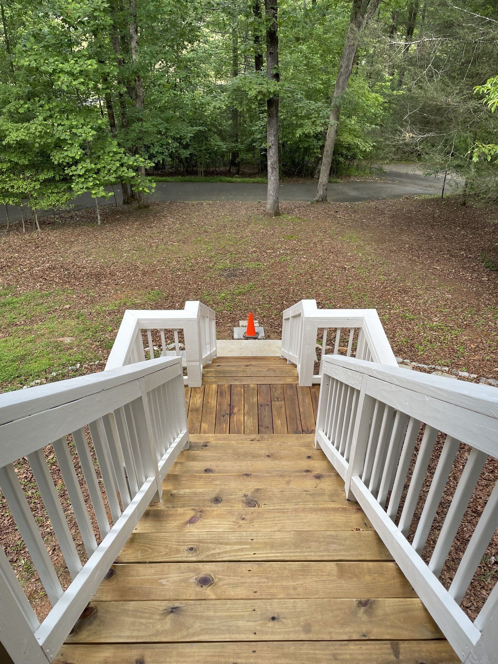 Wooden stairs with white railings lead down to a grassy area in a wooded setting.
