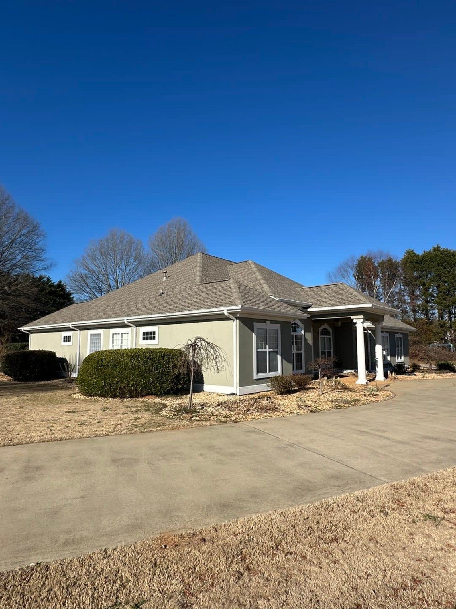 Light green house with a gray roof, white trim, and a long driveway under a clear blue sky.