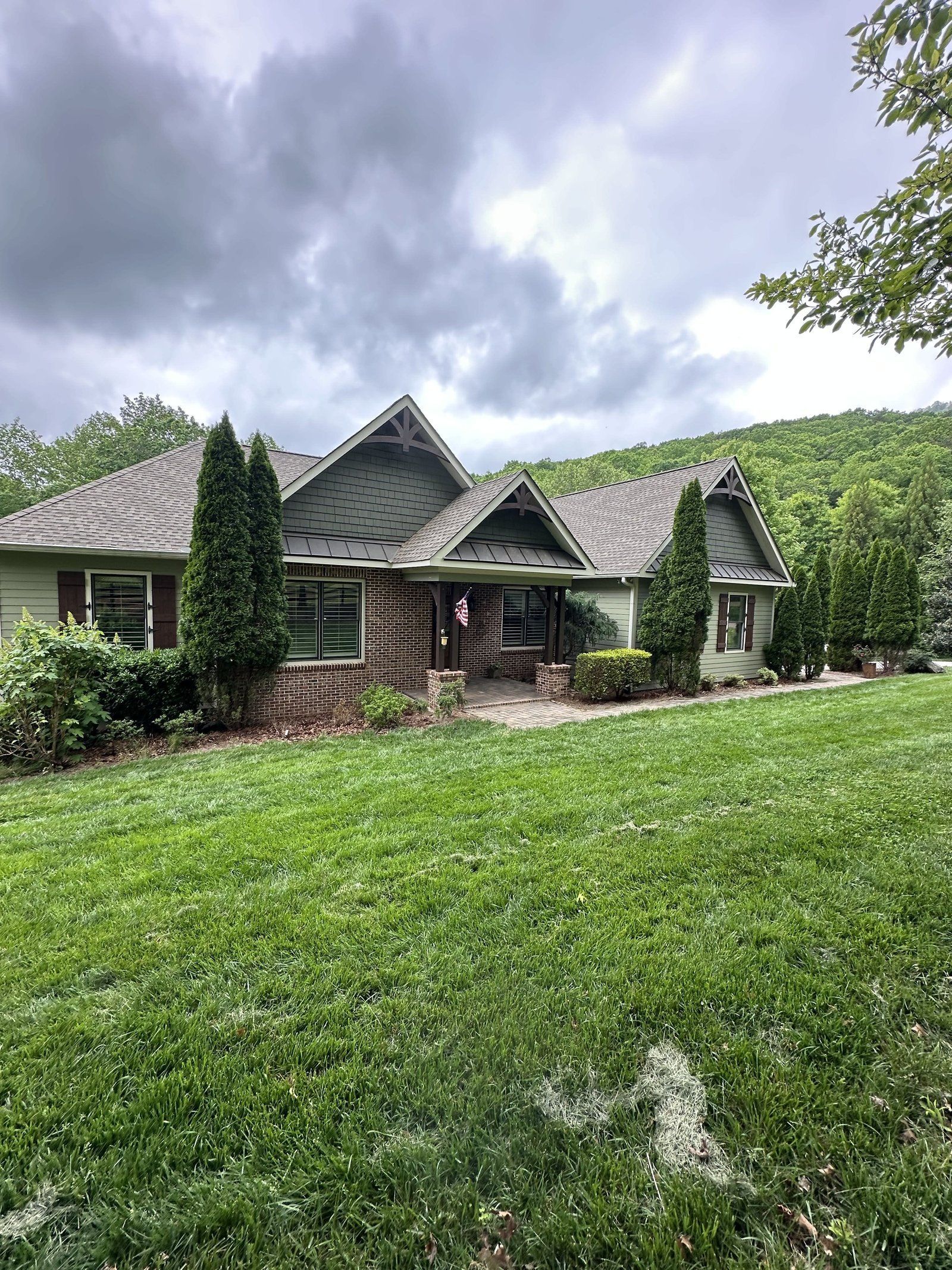 Green house with brown roof, green lawn, trees, and cloudy sky.