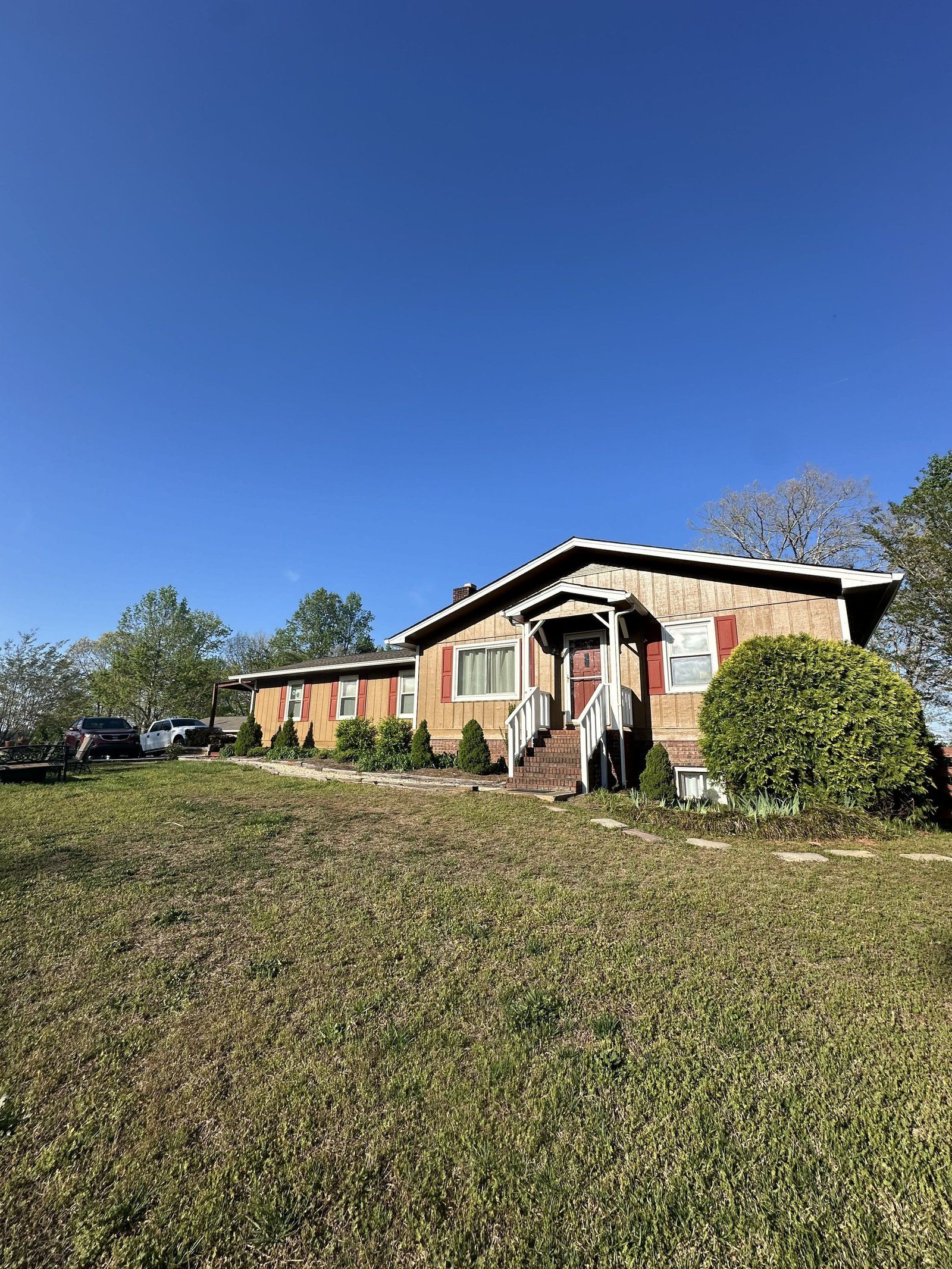 Brown ranch house with a red door, set in a grassy yard under a blue sky.