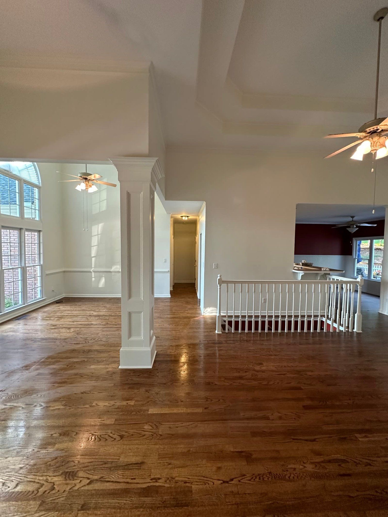 Spacious room with hardwood floors, white walls, and a staircase leading to the kitchen area.