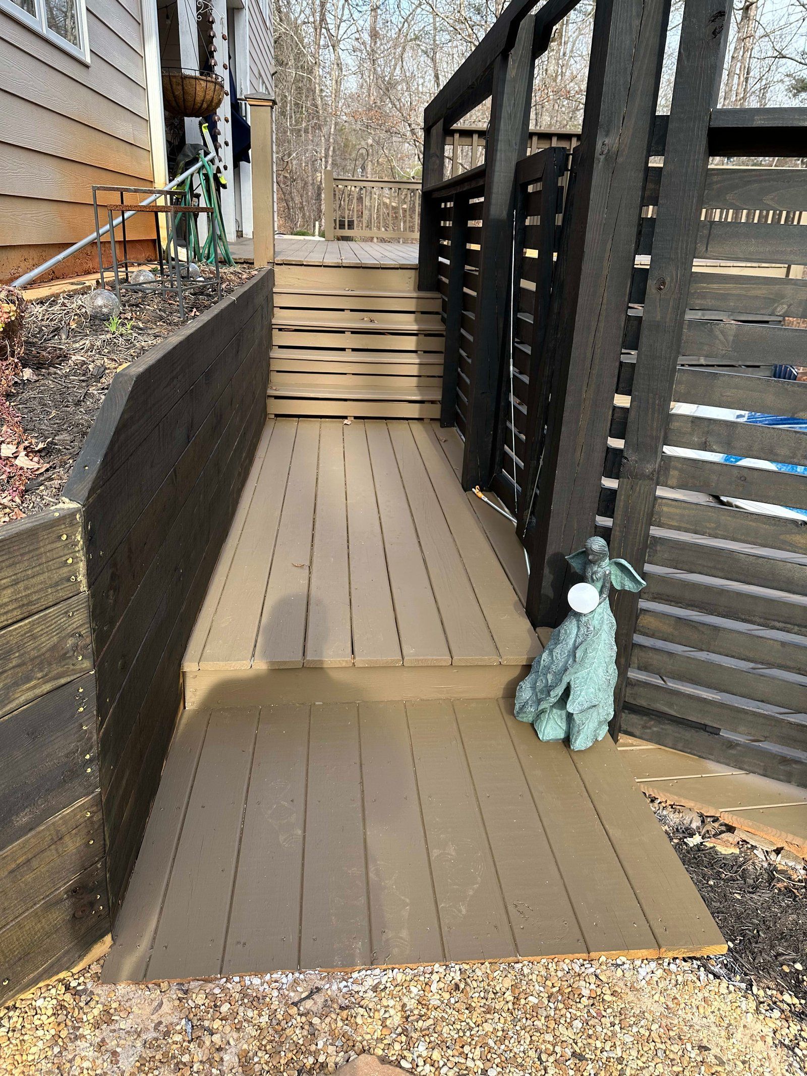 Wooden deck and stairs leading to a higher level, enclosed with a black wooden fence.