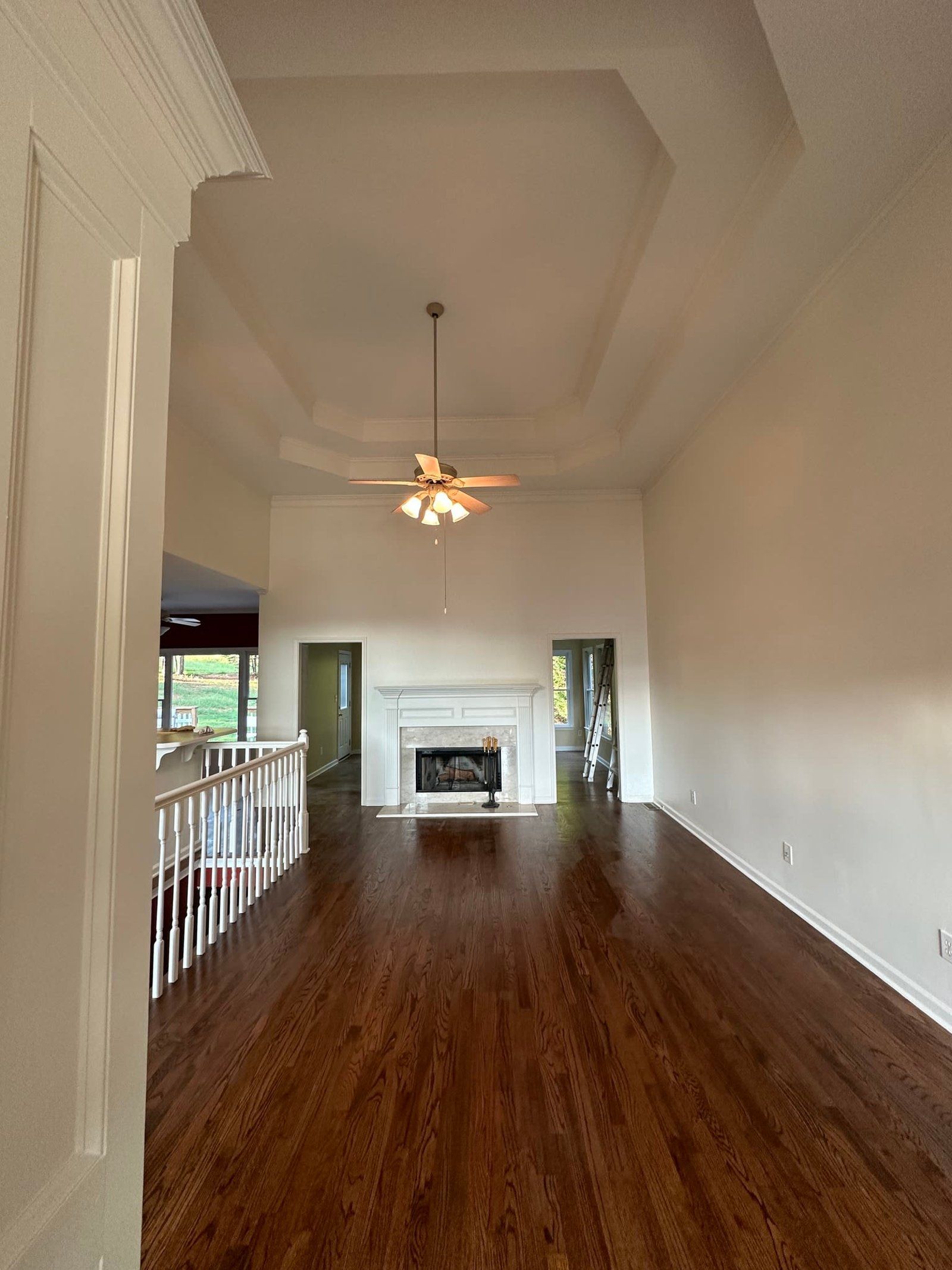 Empty living room with wood floors, fireplace, and high ceiling with a ceiling fan.
