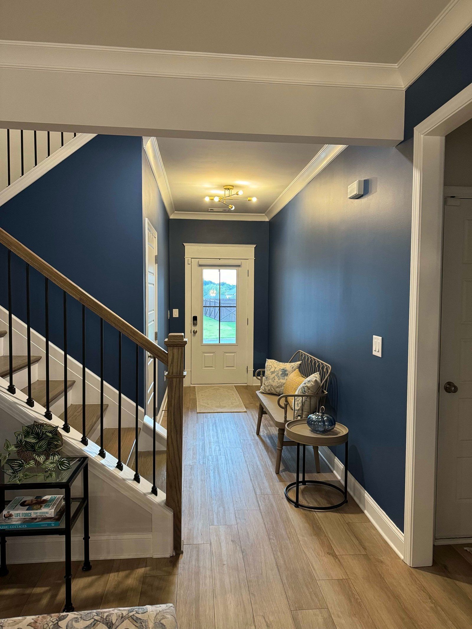 Entryway with blue walls, white trim, wood flooring, staircase, bench, and front door.