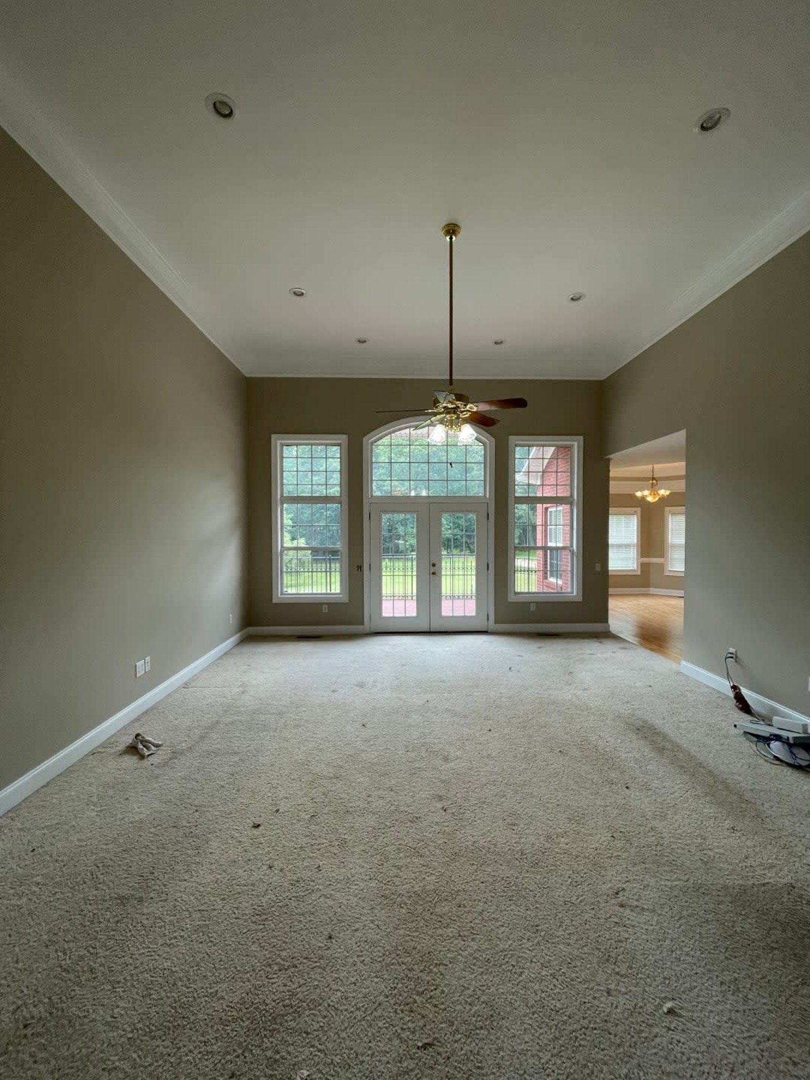 Empty living room with dirty carpet, light brown walls, and large windows.