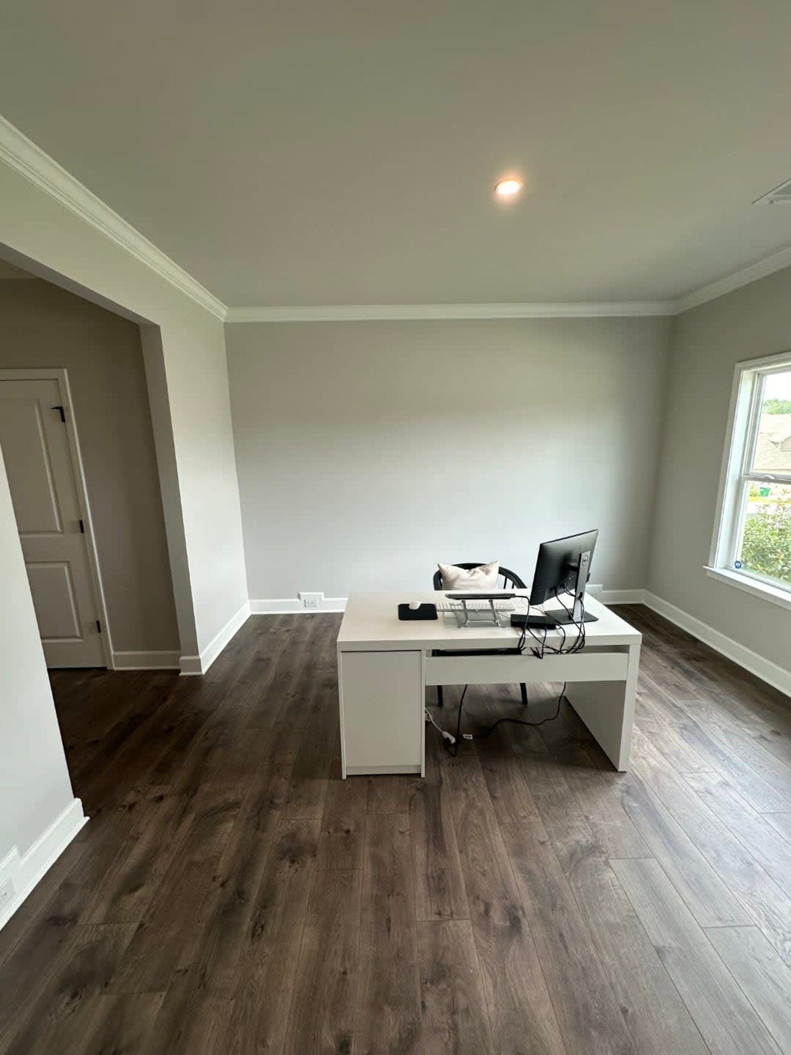 Empty office with white desk, computer, and wood-look flooring. Light gray walls, white trim.