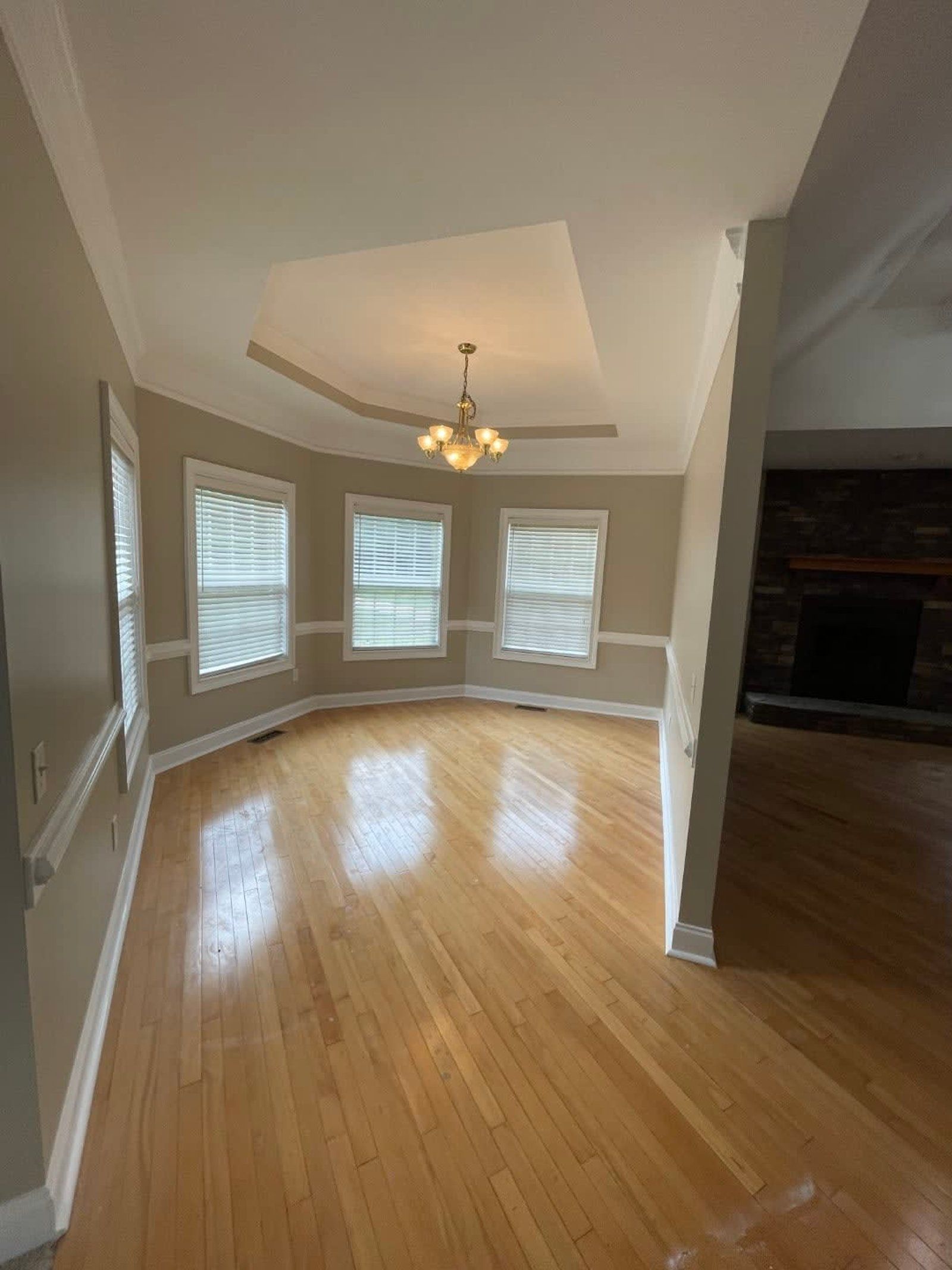 A bright room with wood floors, three windows, a chandelier, and a fireplace.