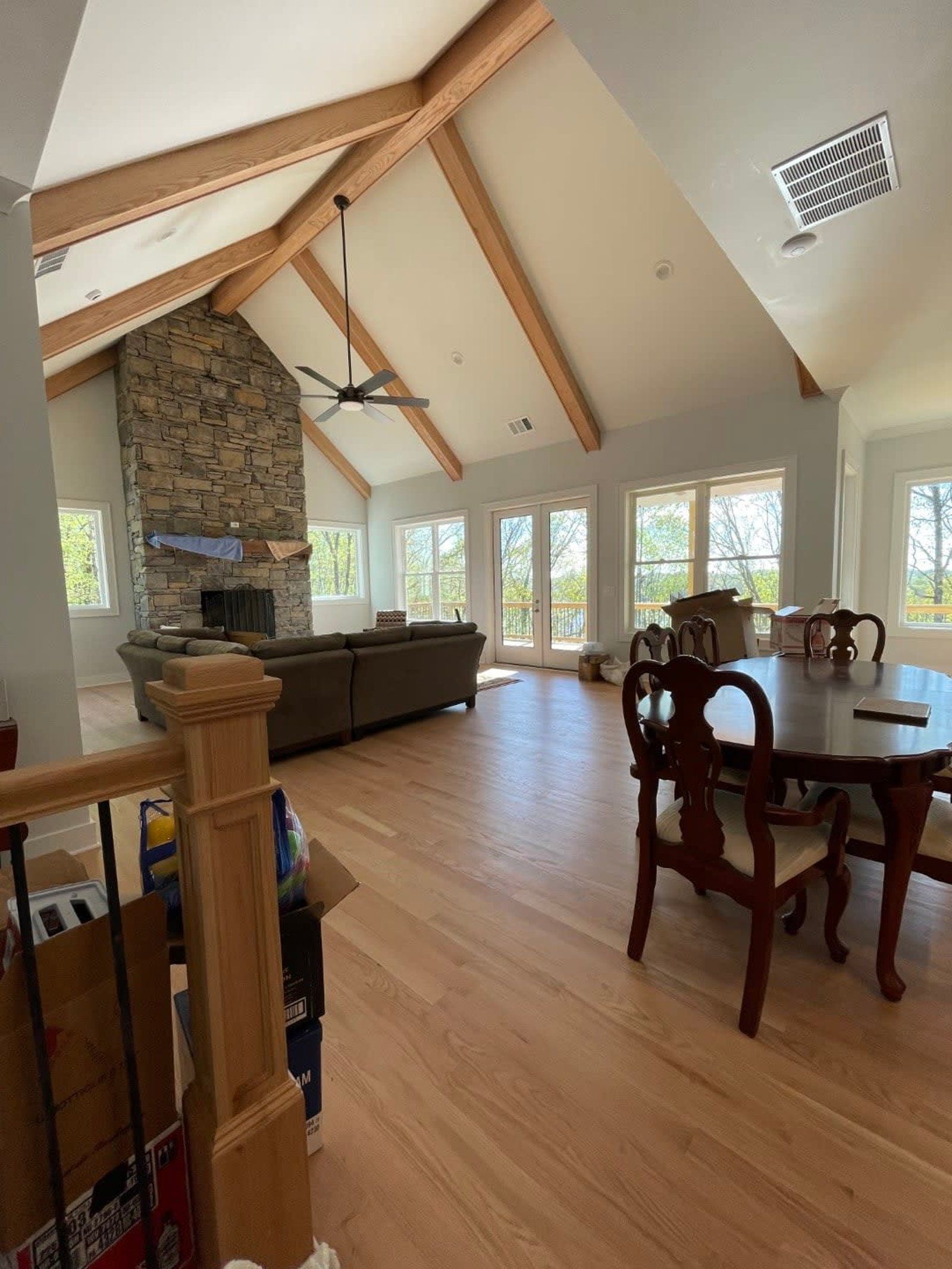 Spacious living area with high vaulted ceiling, exposed wooden beams, stone fireplace, and hardwood floors.
