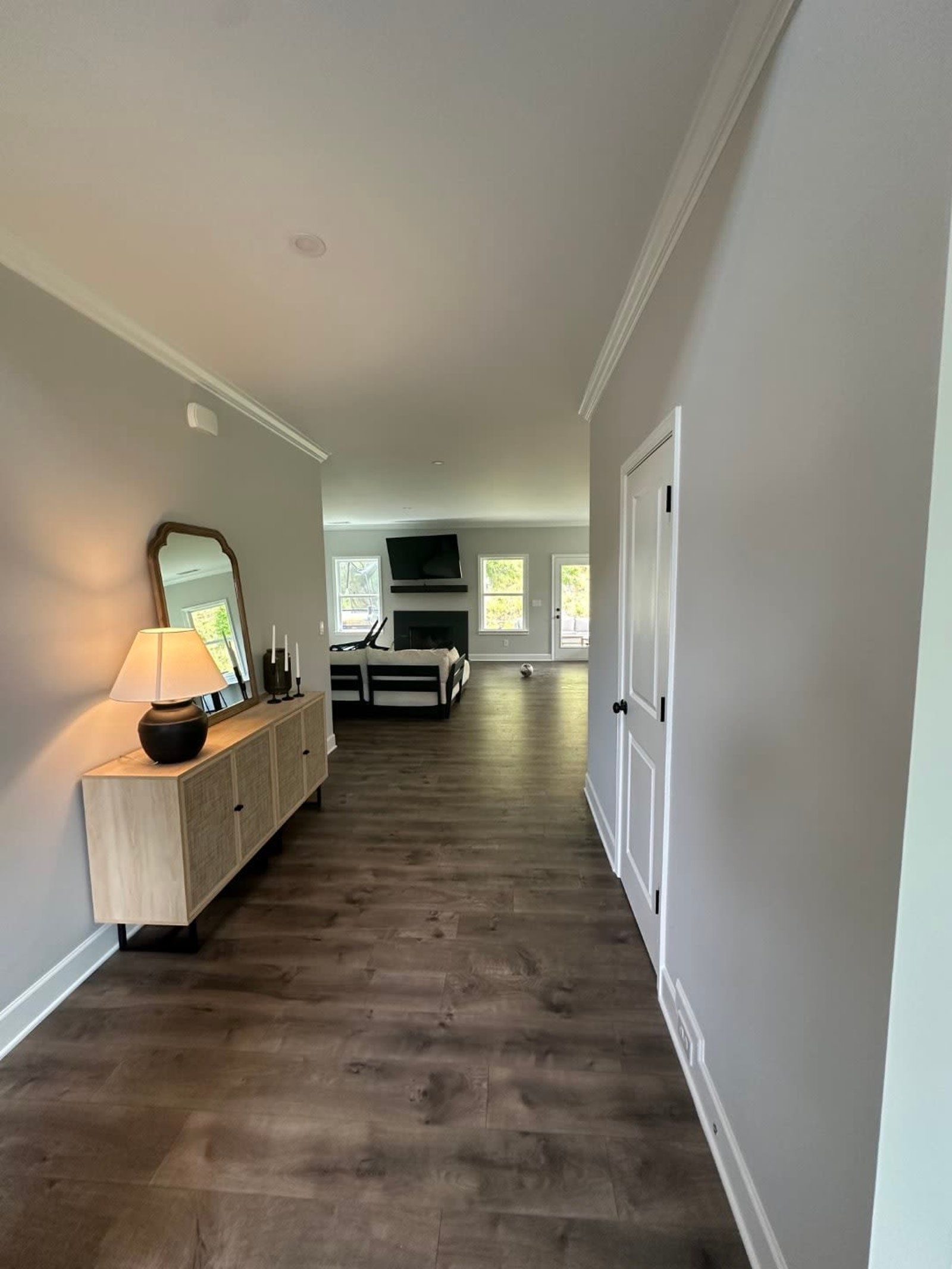 Hallway with light gray walls, dark wood flooring, and a cabinet with a mirror.