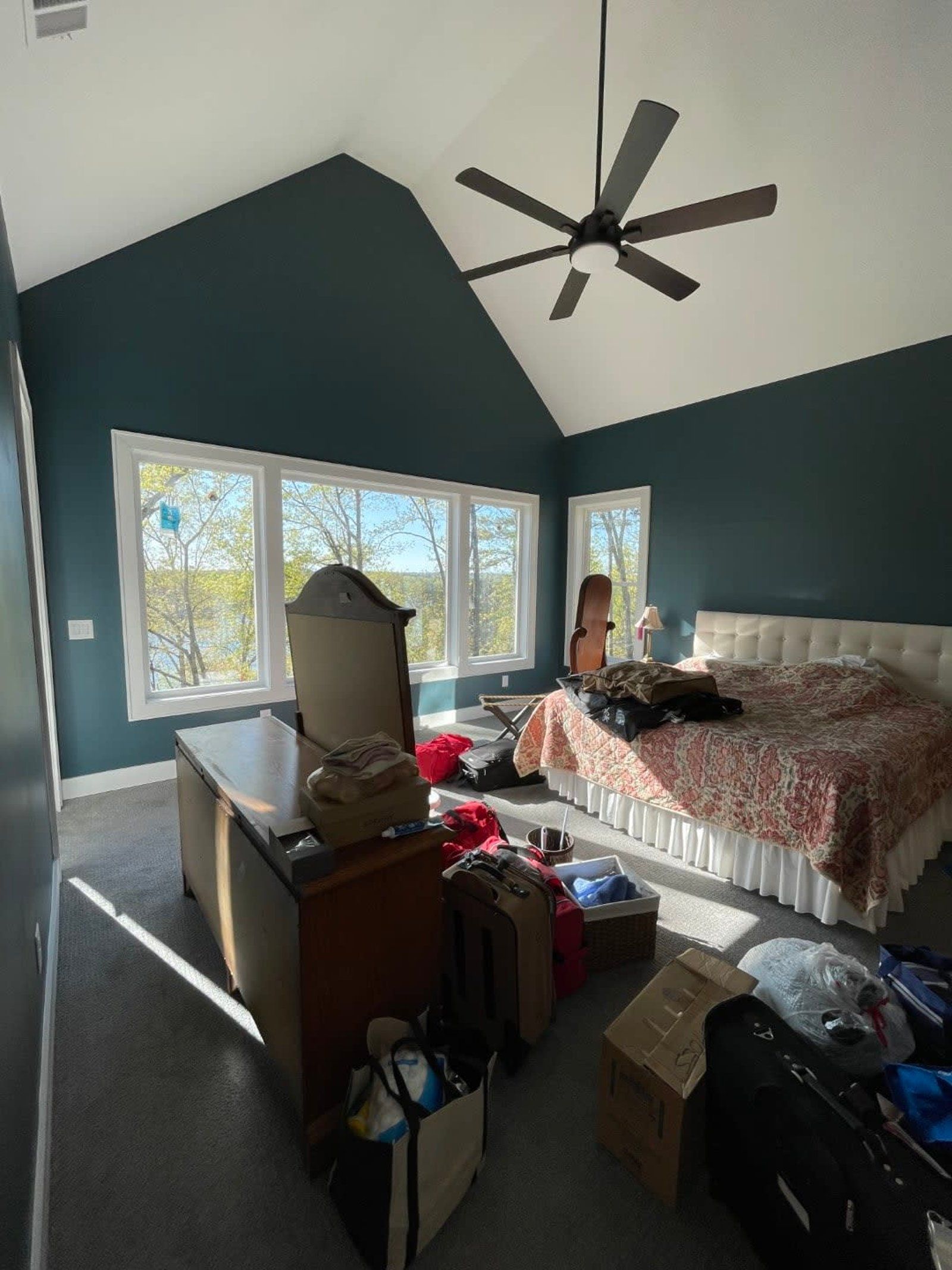 Bedroom with teal walls, a vaulted ceiling, and messy belongings near a window and bed.