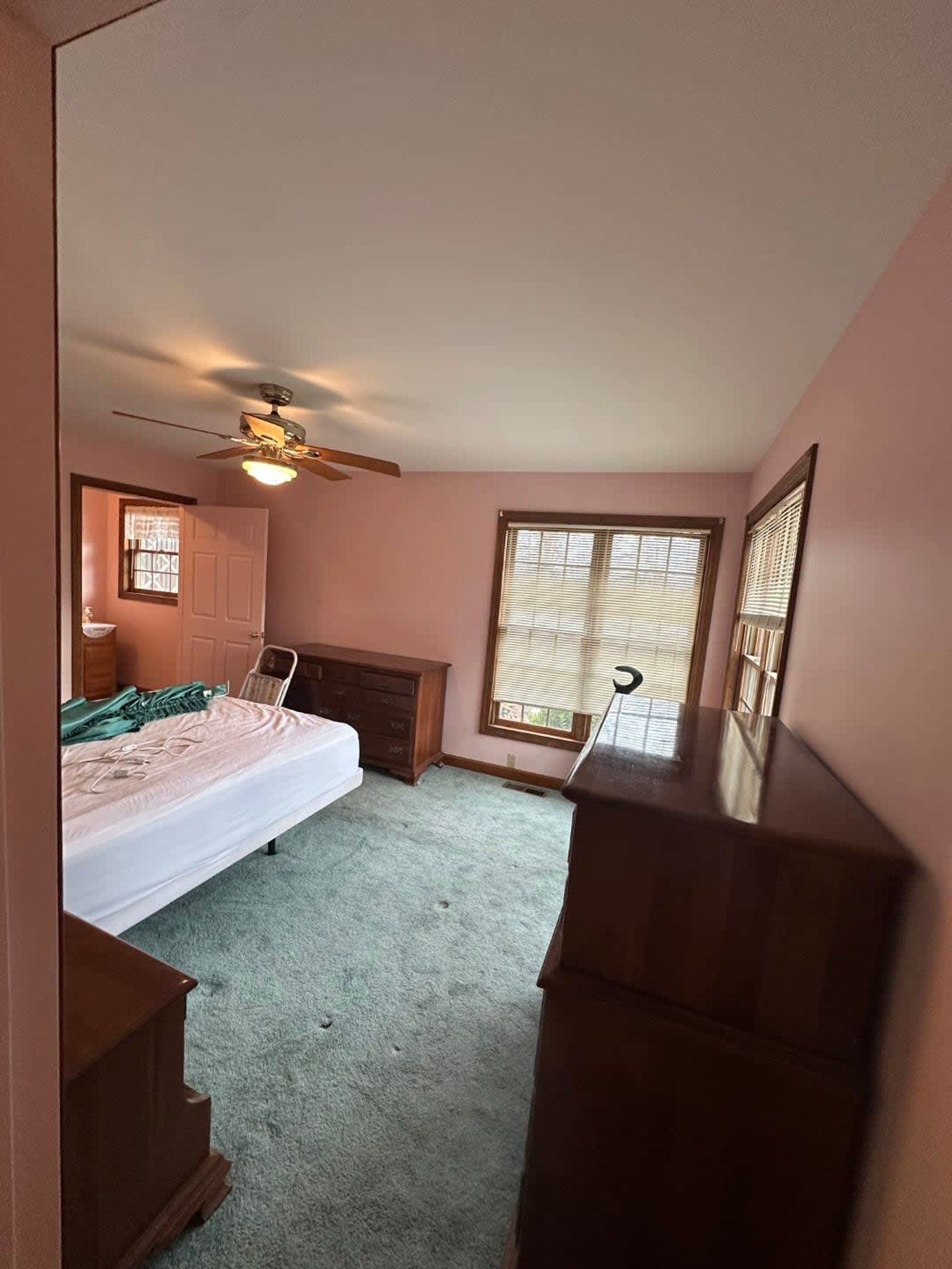 Bedroom with pink walls, green carpet, wood furniture, and a window with blinds.