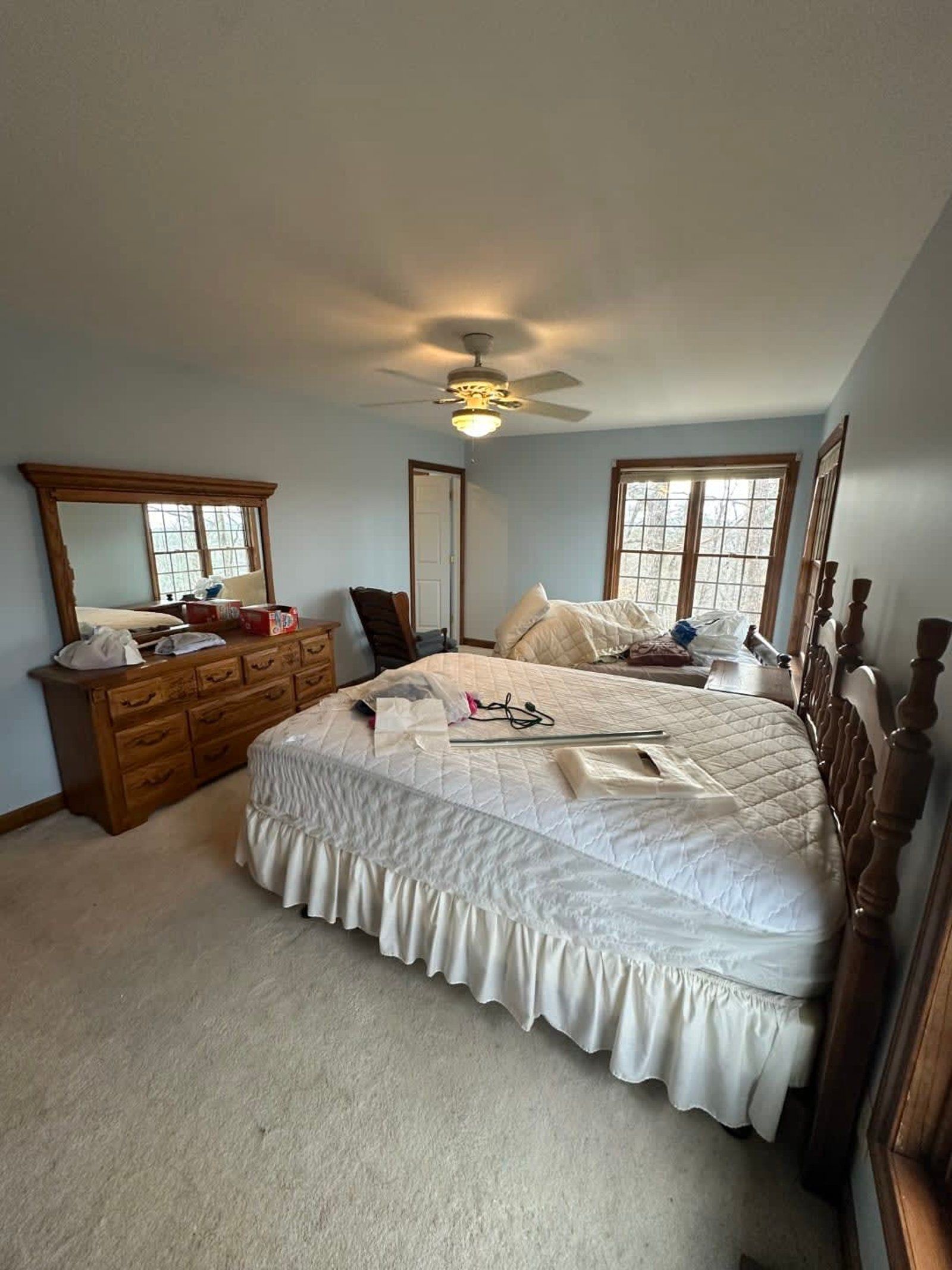 Bedroom with unmade bed, wooden dresser and mirror, light blue walls, and beige carpet.