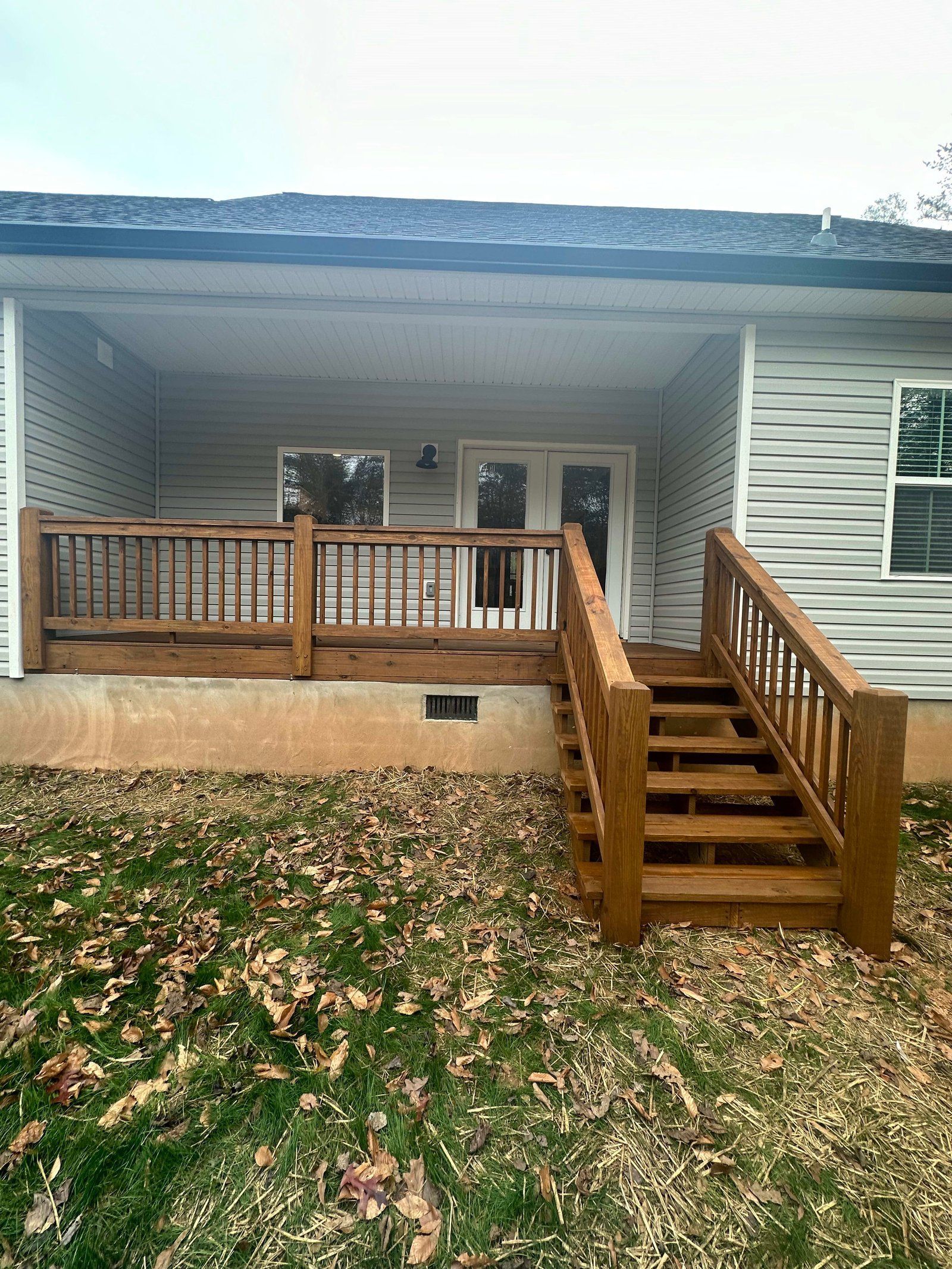 Wooden deck with stairs leading down to a grassy yard. House with light gray siding and covered porch.