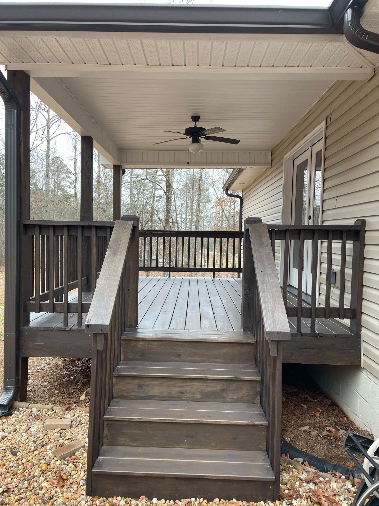 Wooden deck with steps leading up to a covered porch with a ceiling fan. Brown and beige tones.
