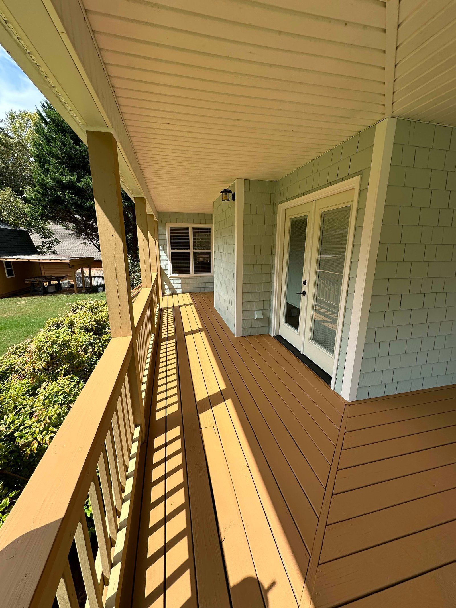 Covered porch with brown flooring, railings, and ceiling. Green siding and white-framed double doors.