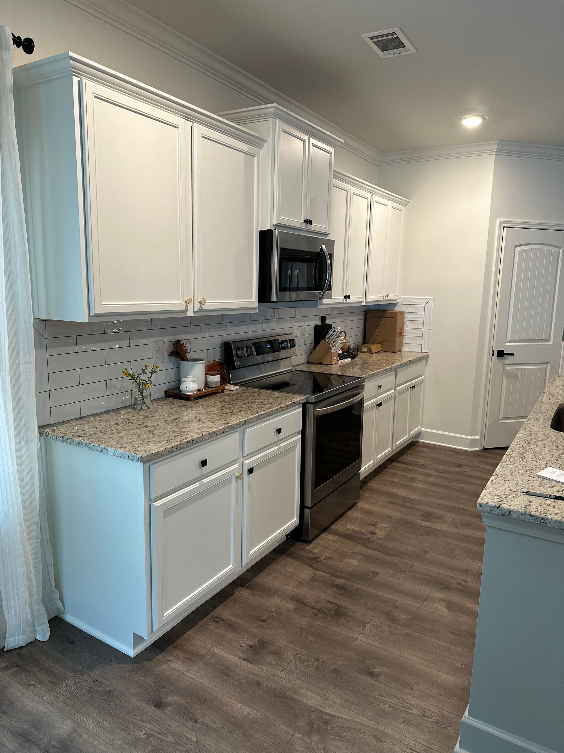 White kitchen cabinets and counters, stainless steel appliances, and wood flooring.