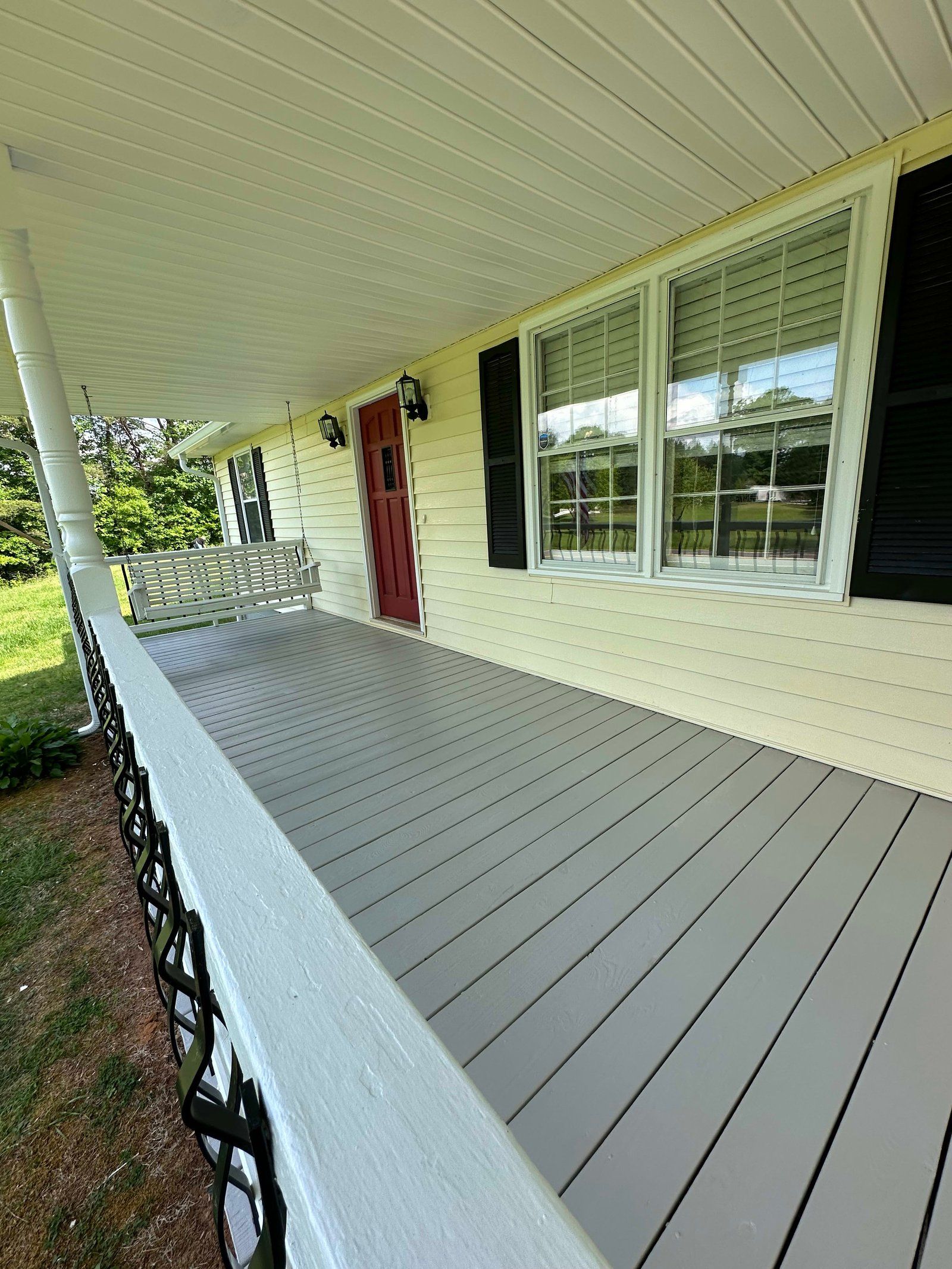 Covered porch with gray deck, white railing and ceiling, red door, and black shutters.