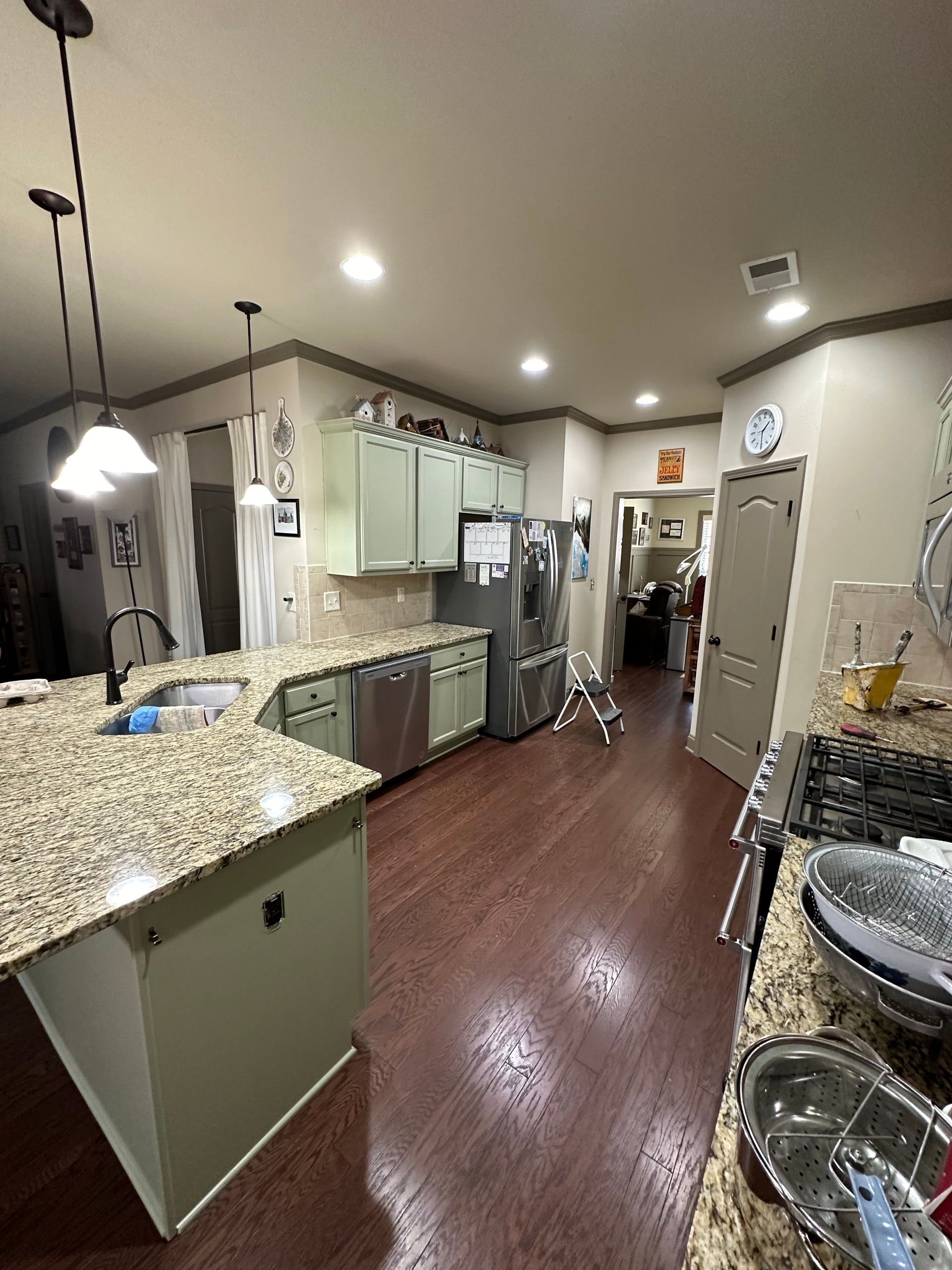 Kitchen with green cabinets, granite countertops, stainless steel appliances, and dark wood floors.