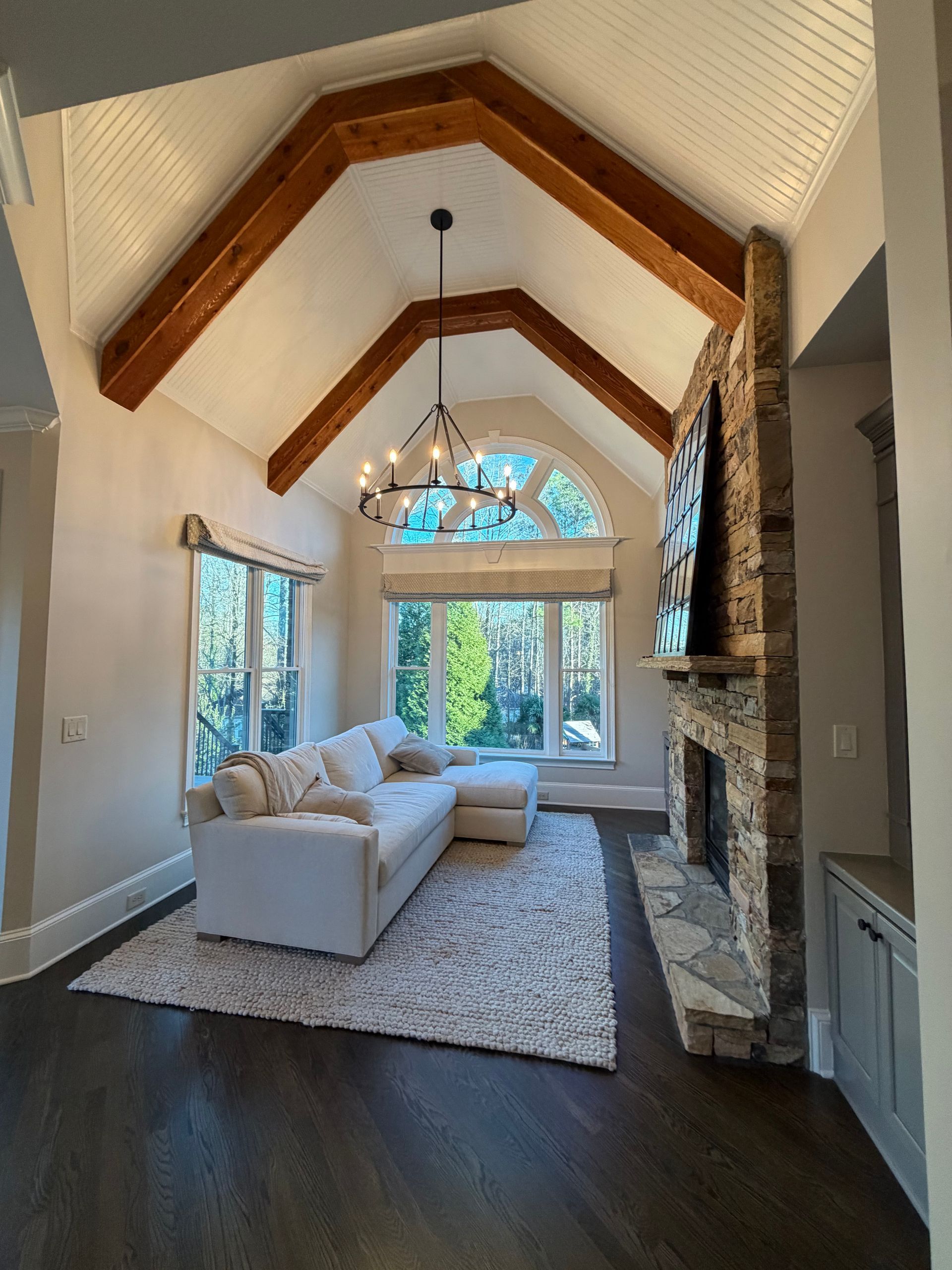 Living room with vaulted ceiling, white walls, stone fireplace, white sectional, and dark wood floors.
