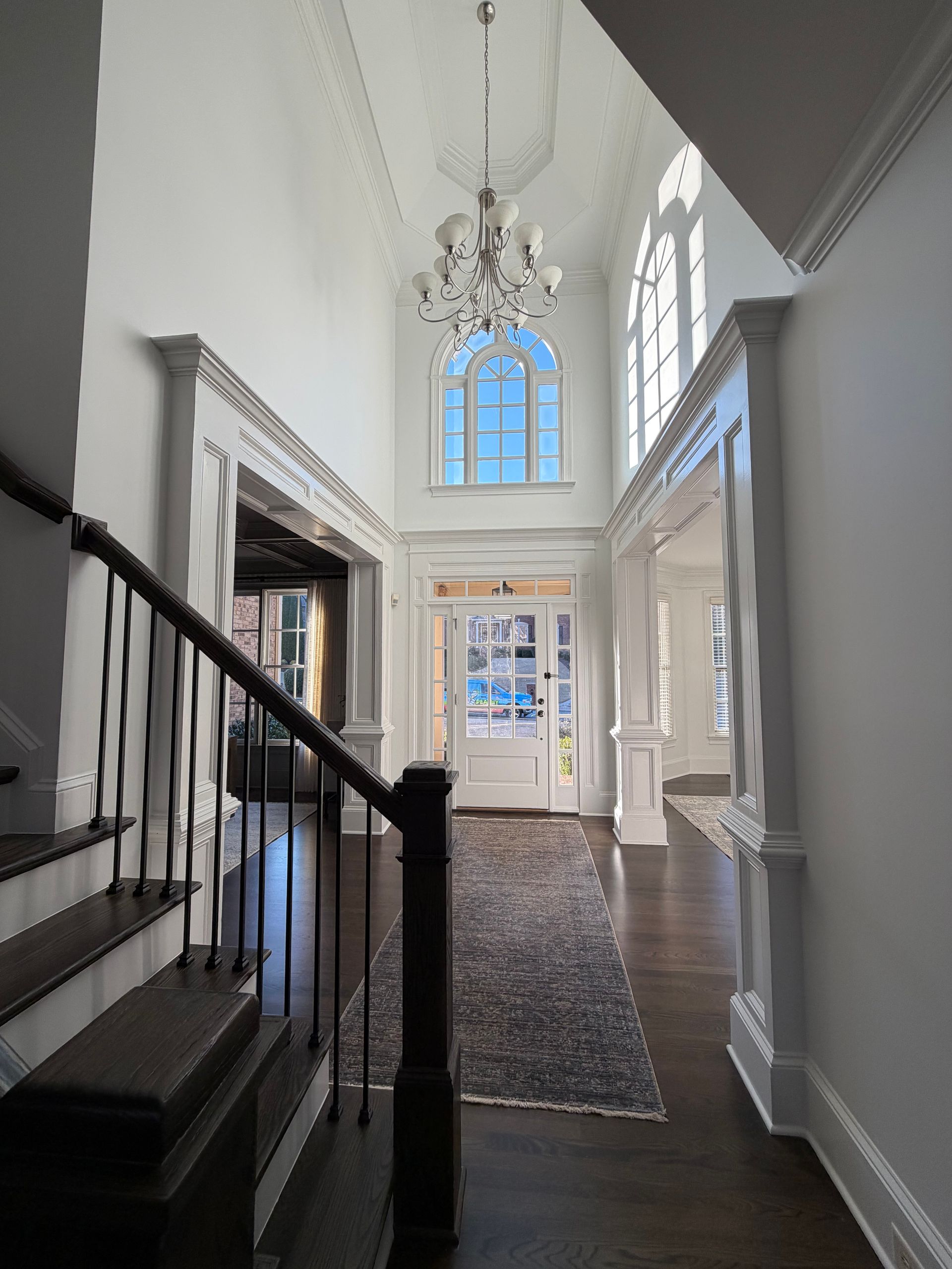 Grand entryway with stairs, dark wood floors, white walls, and a chandelier.