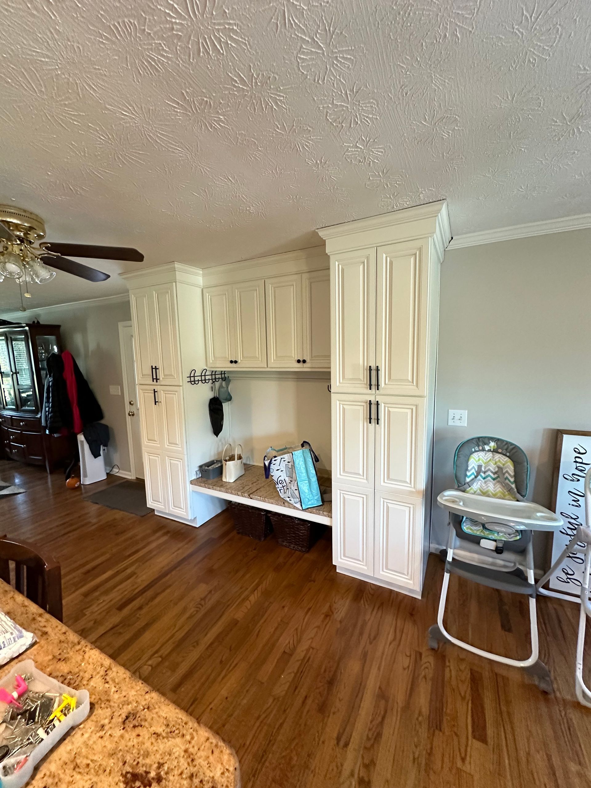 Built-in white storage cabinets with bench and hanging hooks. Hardwood floor. Child's high chair.