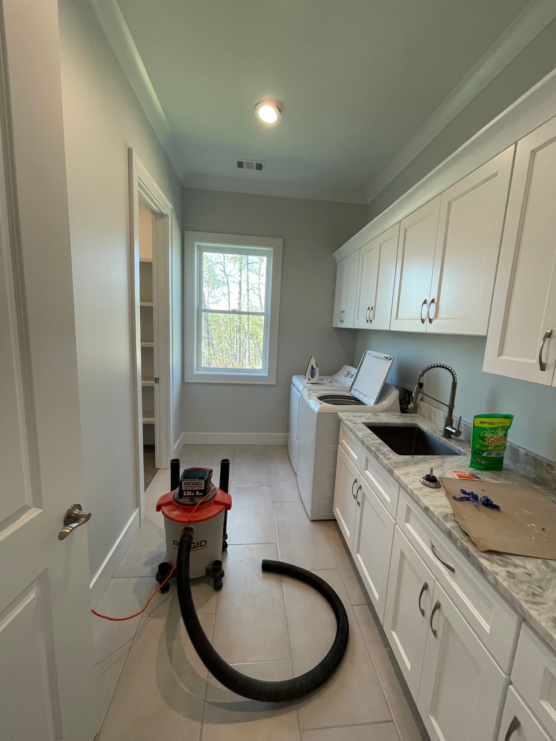 Laundry room with white cabinets, window, washing machine, and a vacuum cleaner.