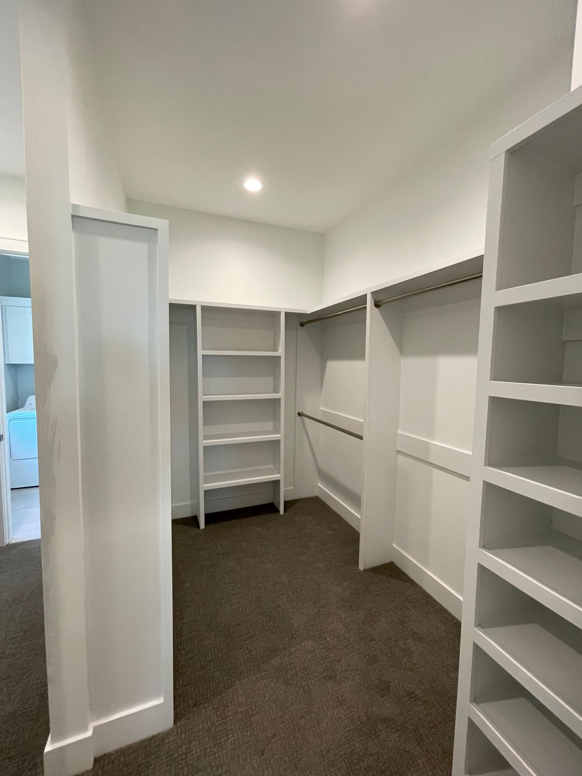 Walk-in closet with white shelves and rods, carpet flooring.