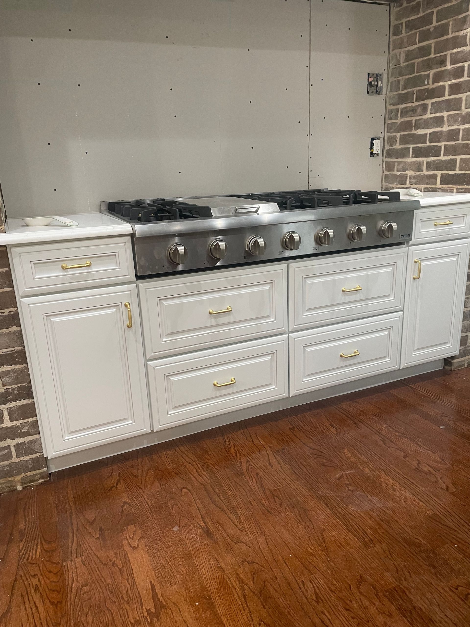 Kitchen with white cabinets, stainless steel range, and brick and drywall walls.