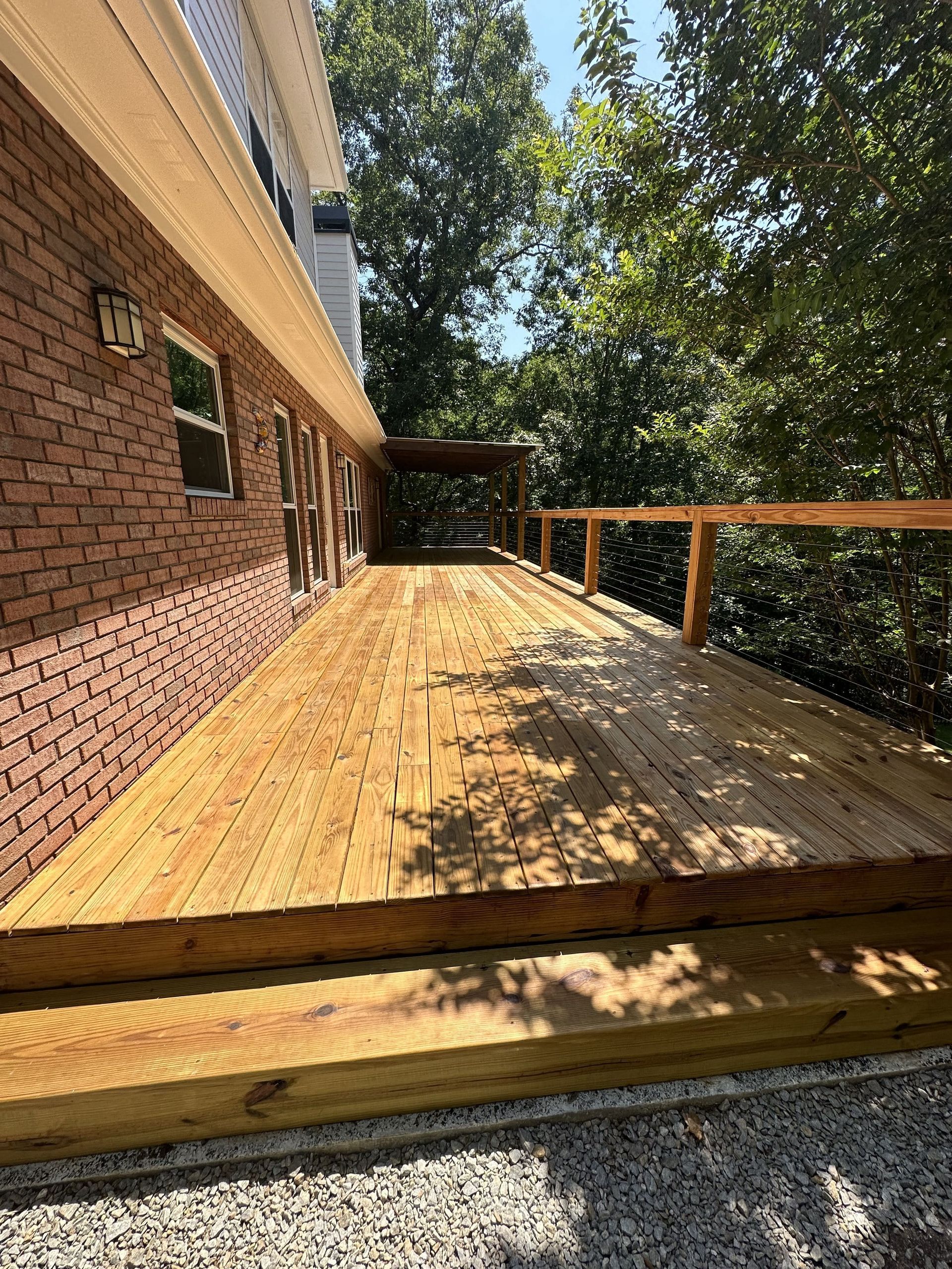 Wooden deck next to a brick building, with a forest background. Sunny outdoor setting.