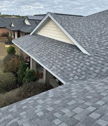 Gray asphalt shingle roofs of multiple houses with beige trim and cloudy sky.