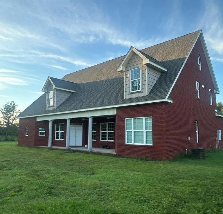 Red brick house with a porch, dormers, and a green lawn under a blue sky.