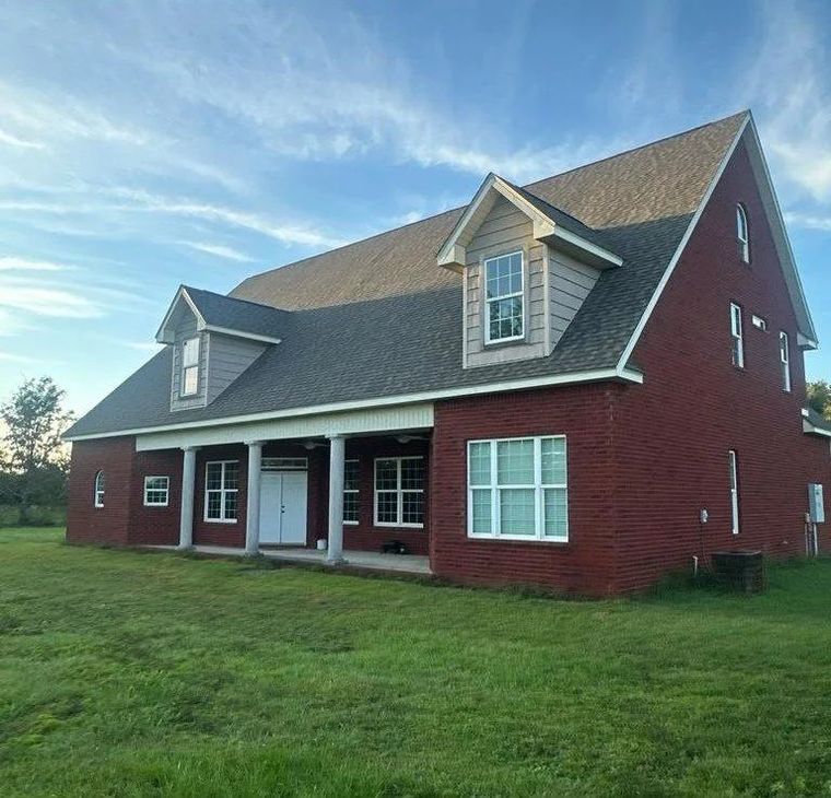 Red brick house with a porch, dormers, and a green lawn under a blue sky.