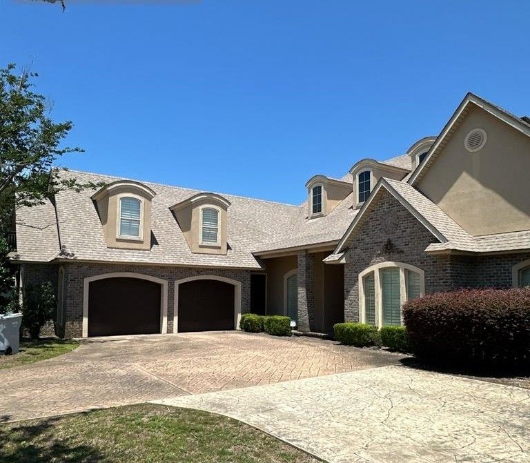 A two-story house with a brick exterior, multiple dormer windows, a shingled roof, and an attached two-car garage.