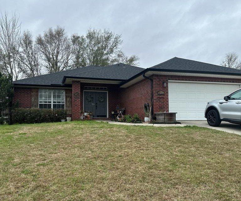 Brick house with black roof and white garage door. Car parked in the driveway. Overcast sky.