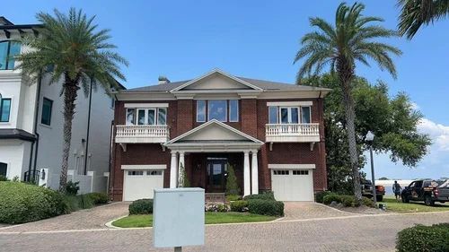 Two-story brick house with white trim, two palm trees, two garage doors, and a front porch.