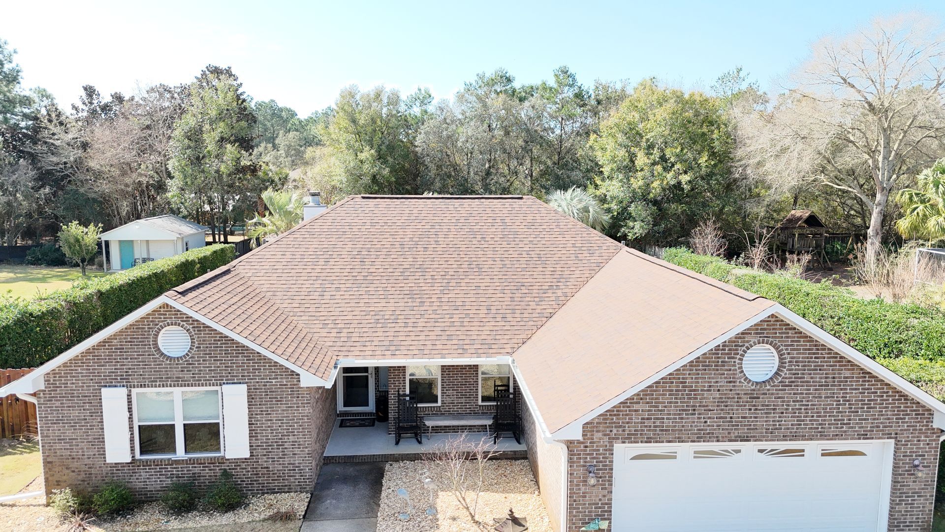 A single-story brick house with a brown shingled roof, white shutters, and an attached two-car garage.