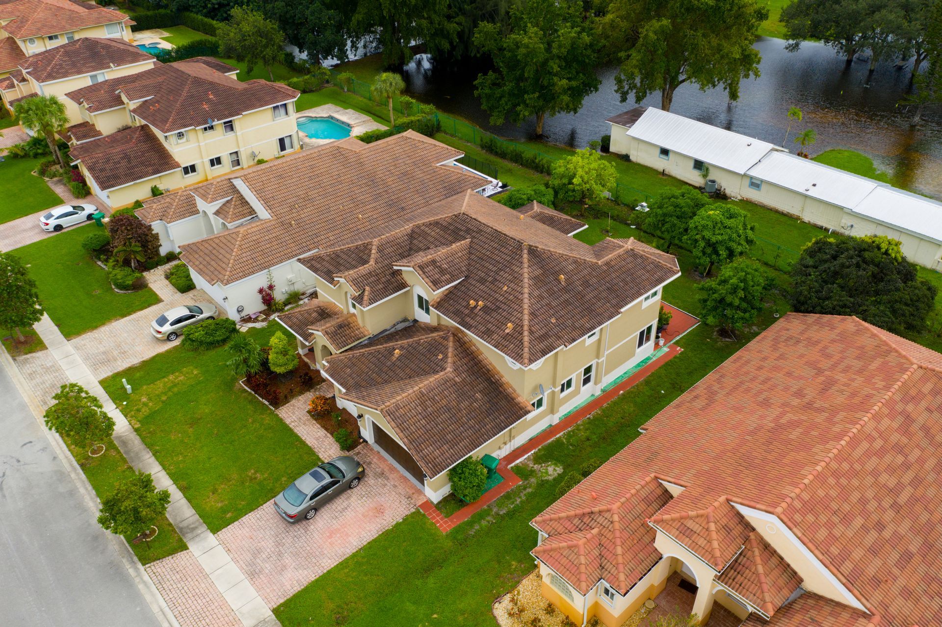 Aerial view of houses with brown tile roofs, green lawns, and a blue pool.