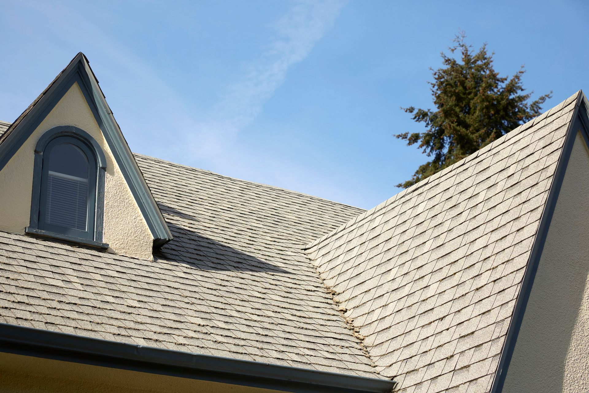 A gray shingled roof with a dormer, against a blue sky.