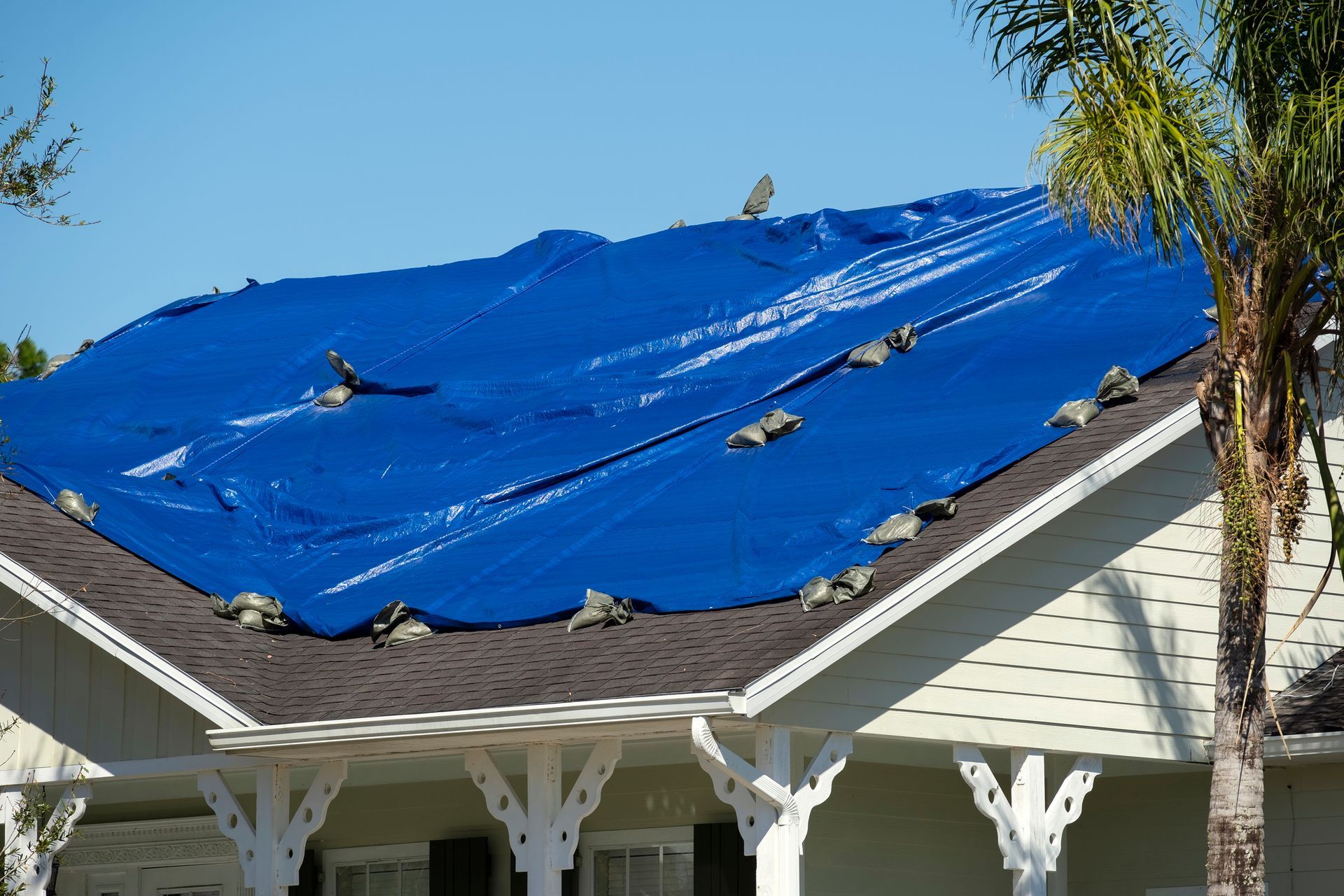 Blue tarp covers a house roof, weighted down with rocks.
