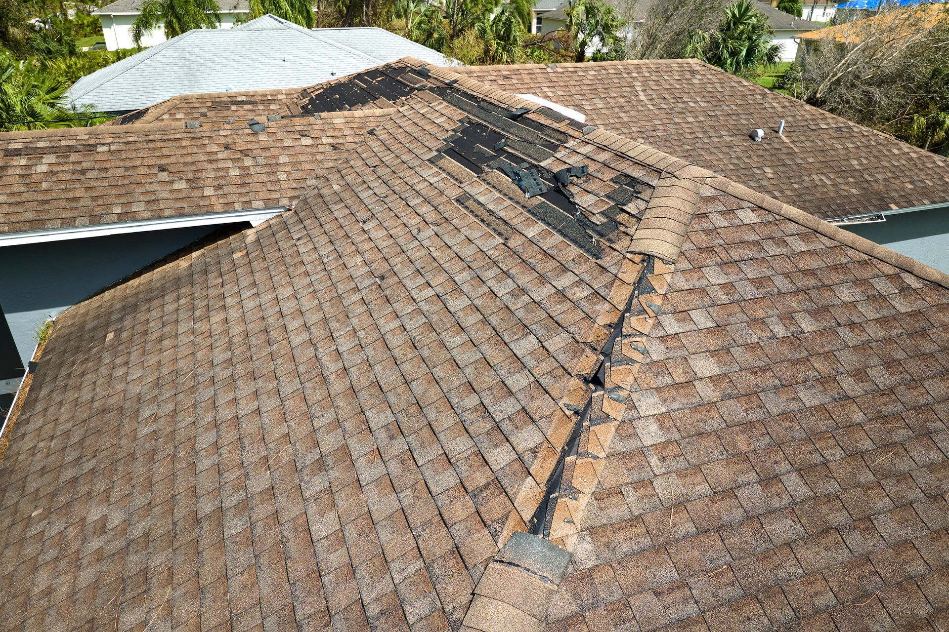 A damaged brown shingle roof with missing sections, seen from above.