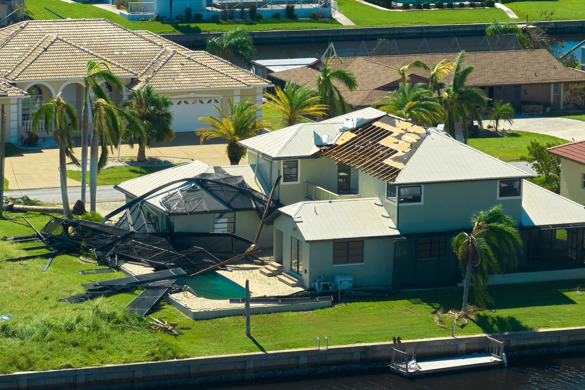 A house with severe roof damage and a collapsed pool cage after a storm.