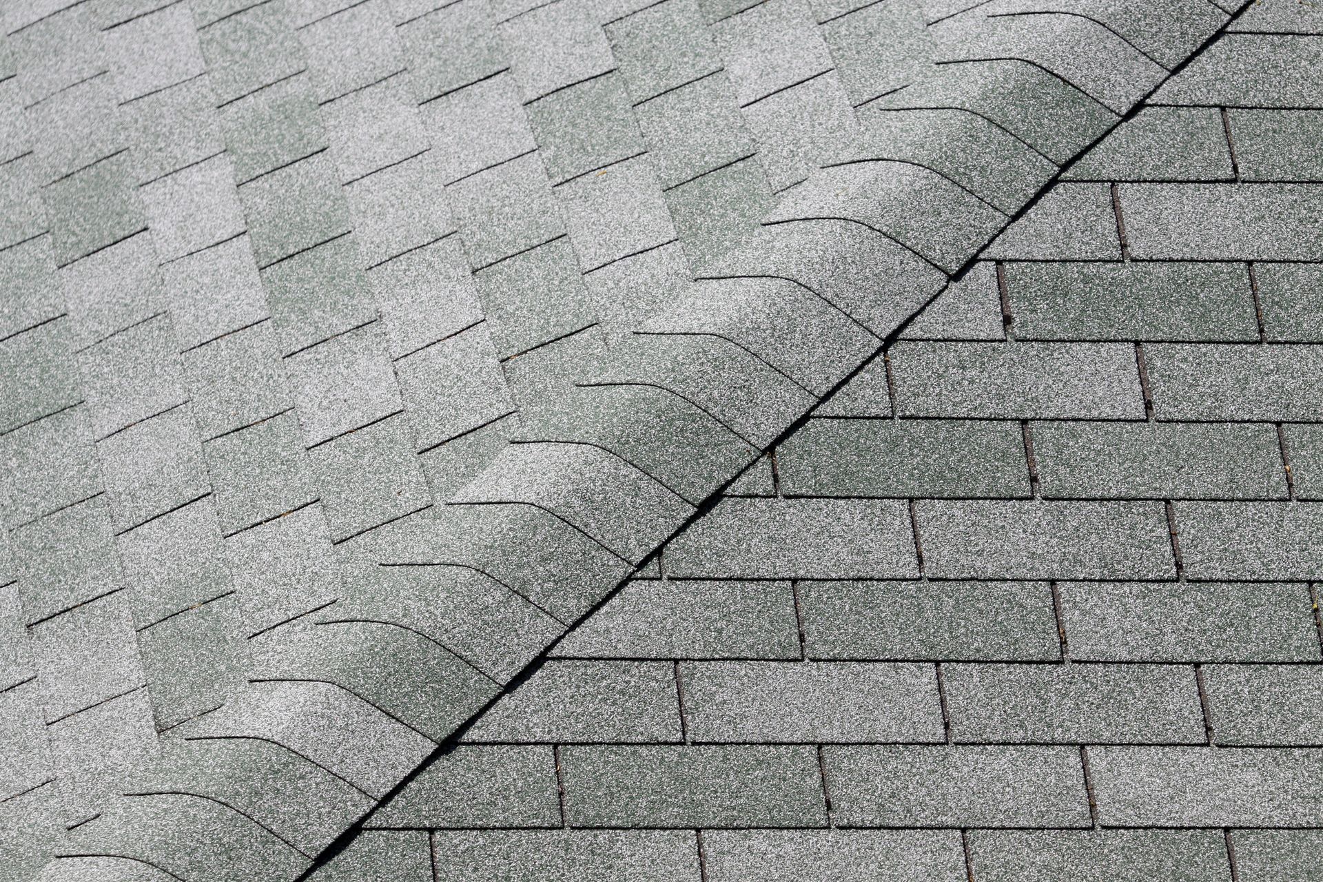 Overhead view of a roof with two different styles of gray shingles meeting at a diagonal line.