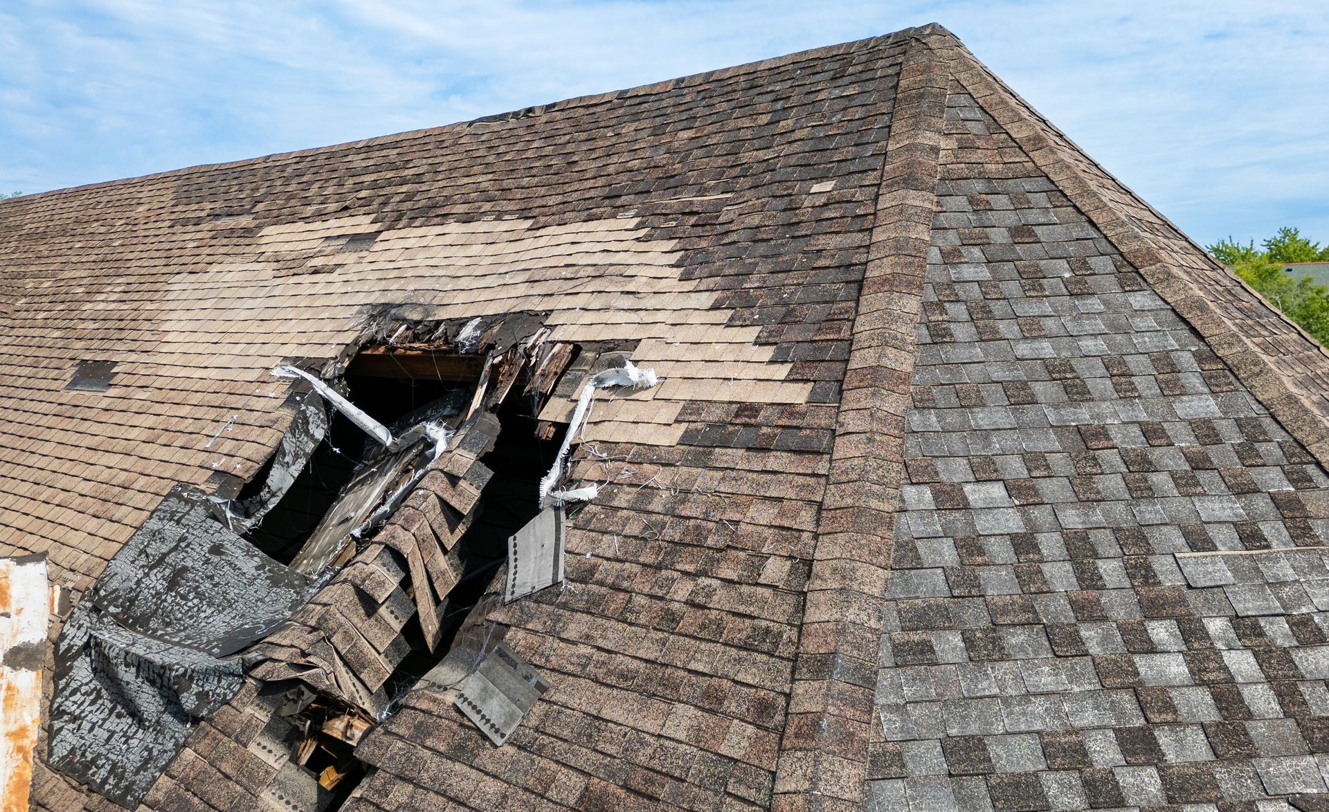 Damaged asphalt shingle roof with a large hole.
