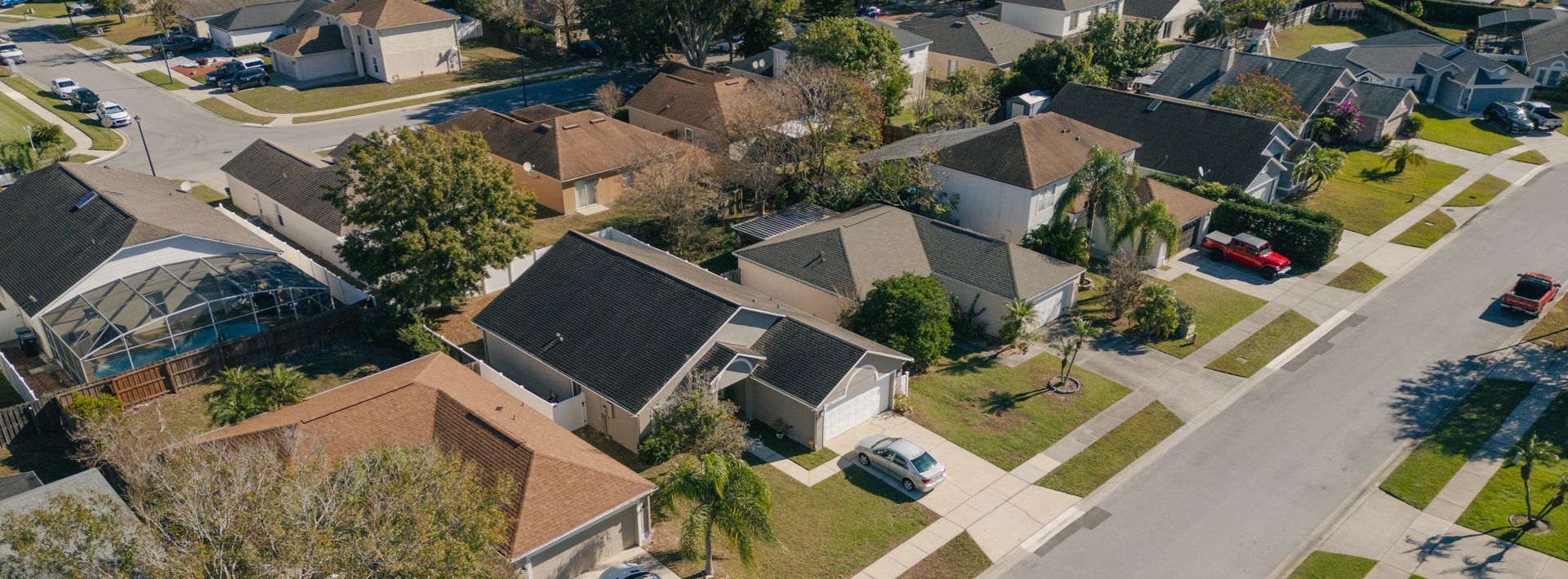 Aerial view of a suburban neighborhood with houses, driveways, streets, and green lawns.